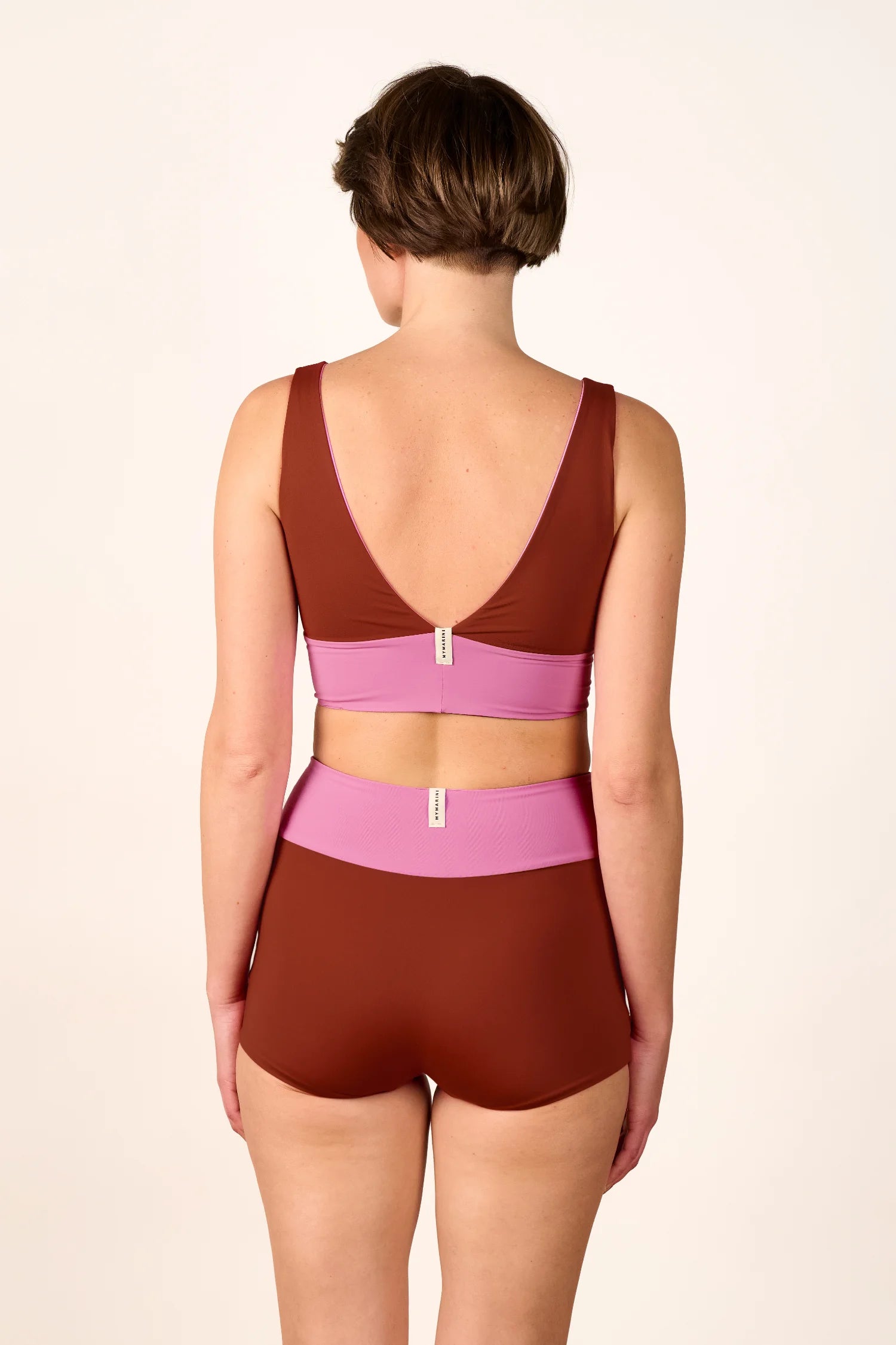 Rückansicht einer Frau in MYMARINI Bikinihose und Bikinitop mit V-Ausschnitt und breiten Trägern in Braun und Rosa.#color_sienna-orchid