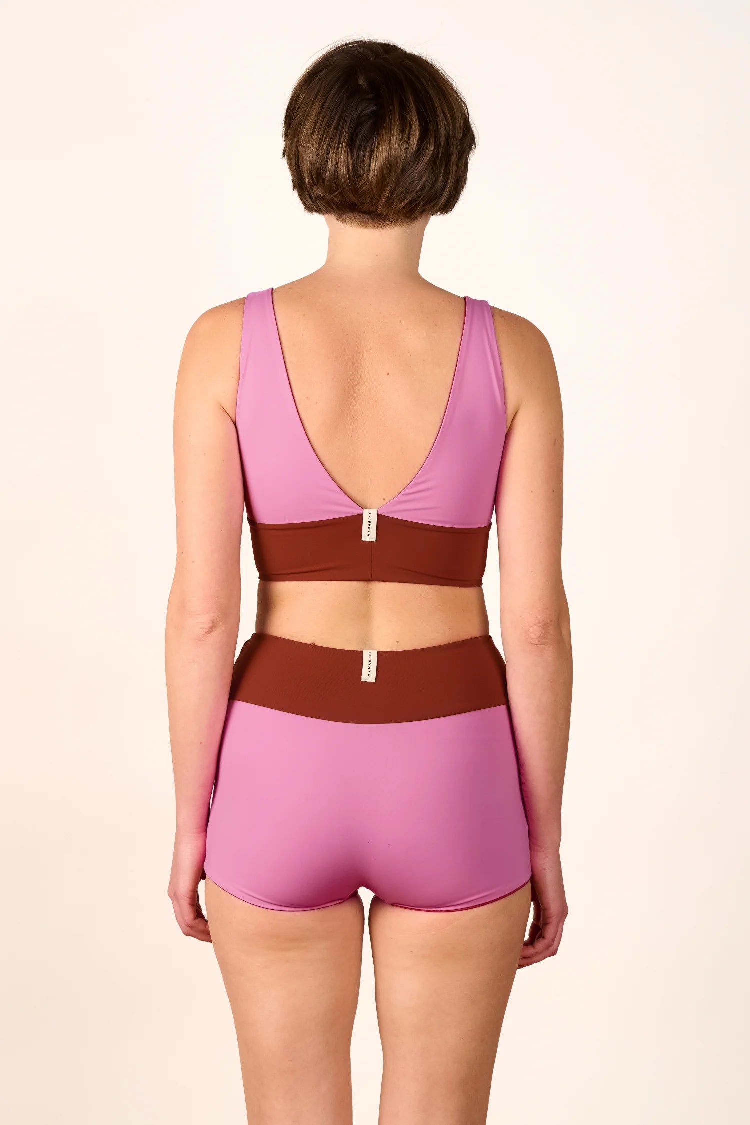 Rückansicht einer Frau in einem MYMARINI Bikini mit V-Ausschnitt und High Waist Schnitt in Rosa und Braun.#color_sienna-orchid
