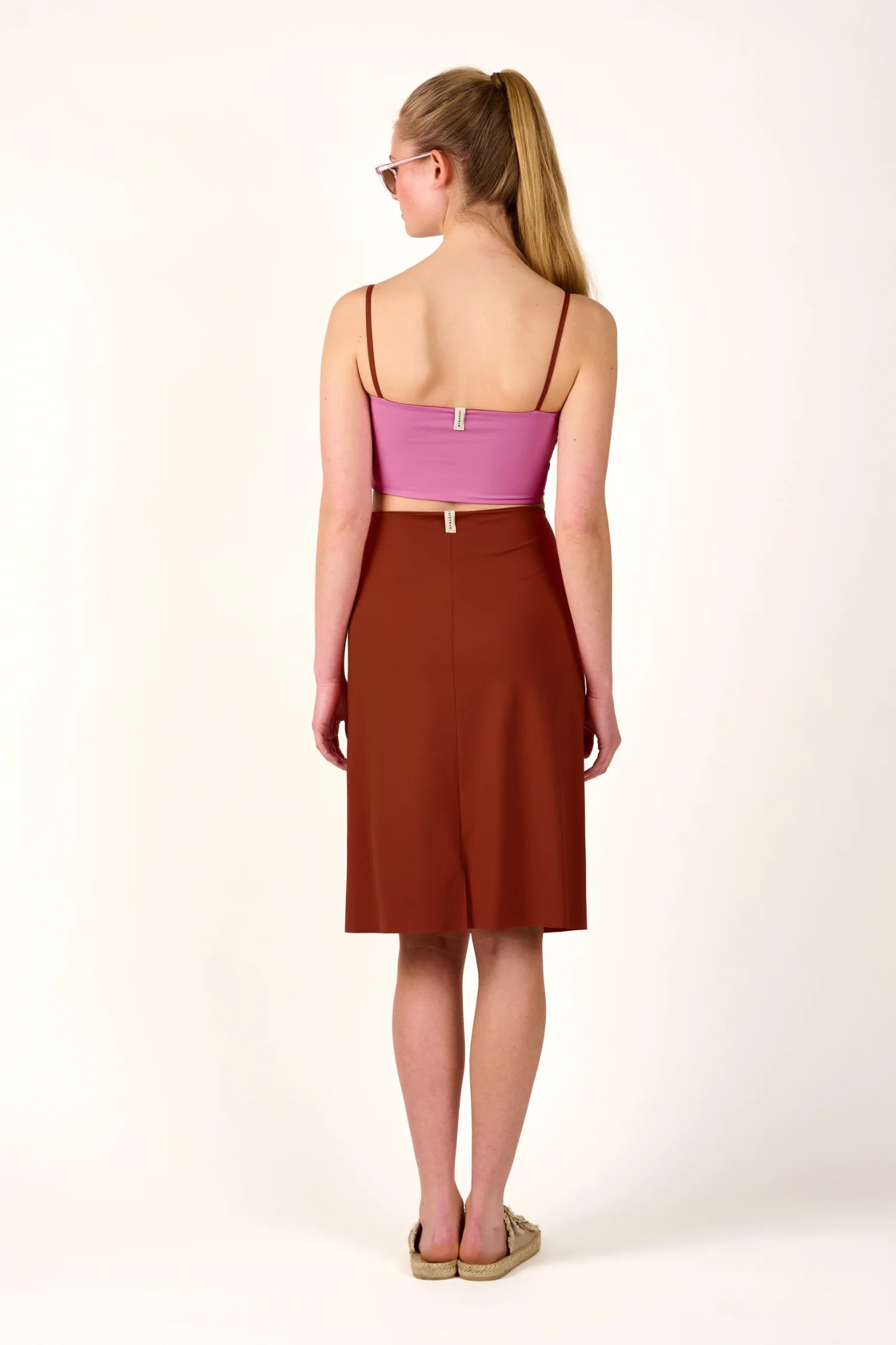 Frau in rosa MYMARINI-Bikinitop mit Spaghettiträgern und braunem Rock, von hinten, vor weißem Hintergrund.#color_sienna