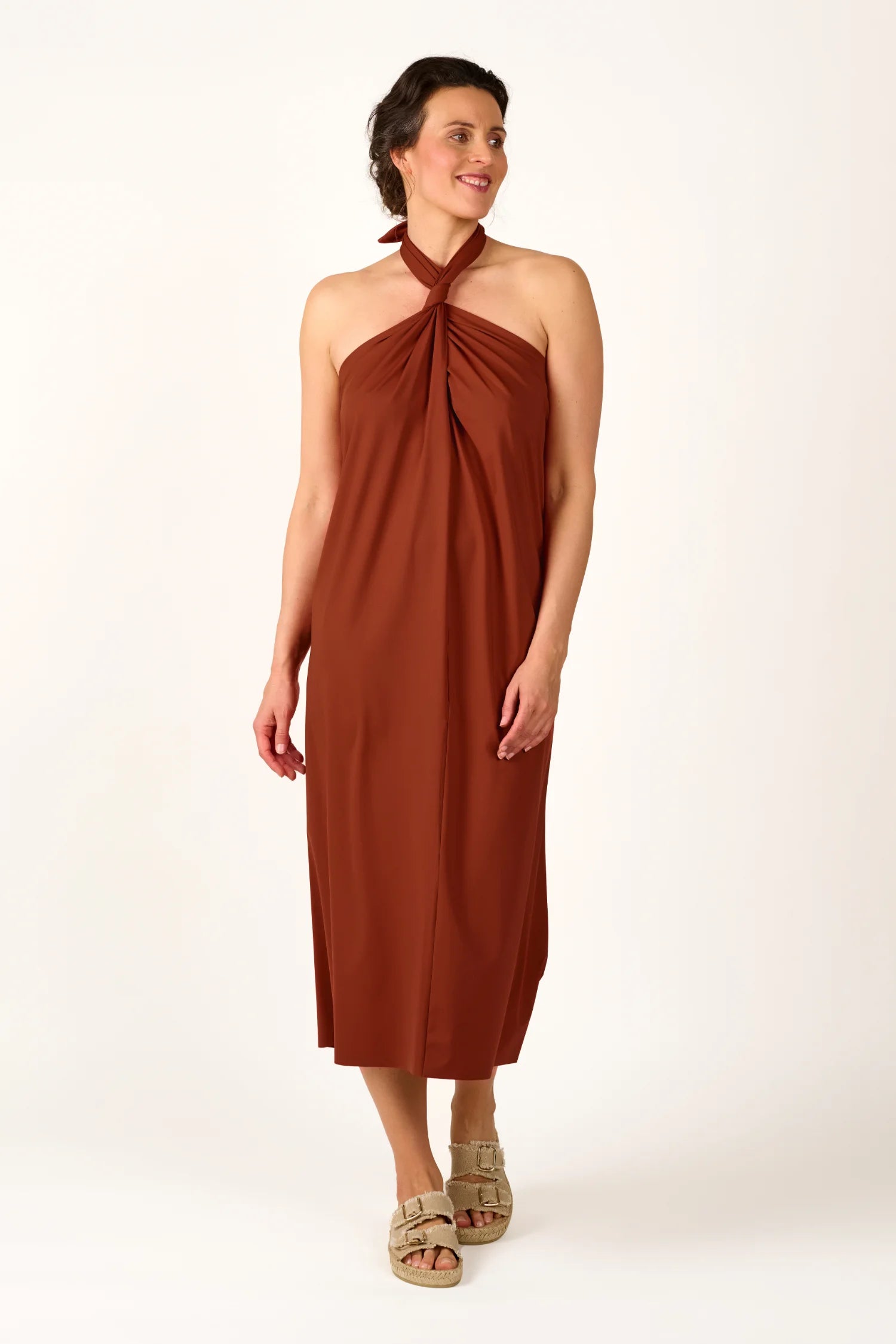 Frau trägt ein braunes MYMARINI Neckholder-Kleid, stehend, mit Sandalen.#color_sienna