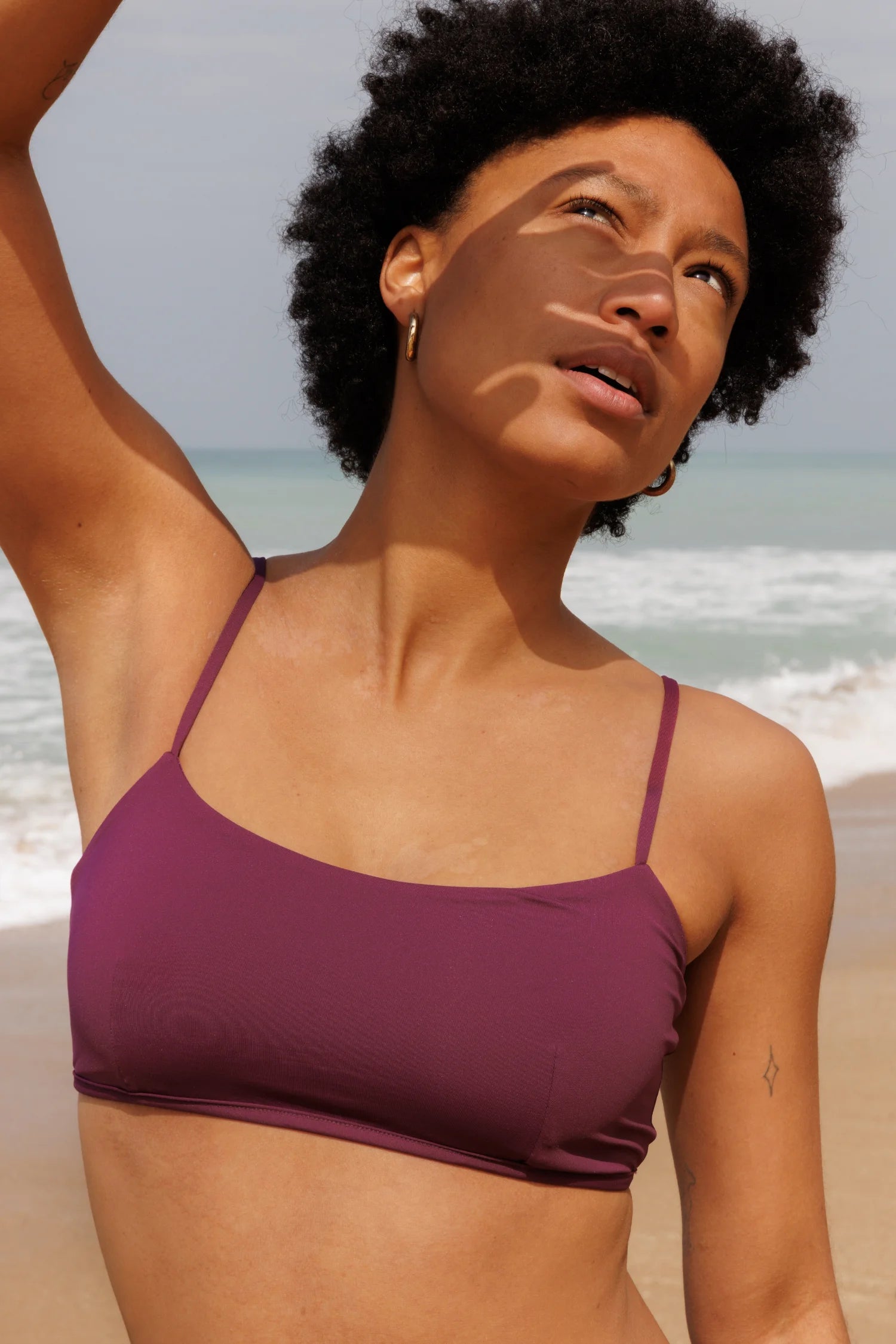 Bikinitop von MYMARINI in Lila mit schmalen Trägern, getragen von einer Person am Strand, im Sonnenlicht.#color_berry-print
