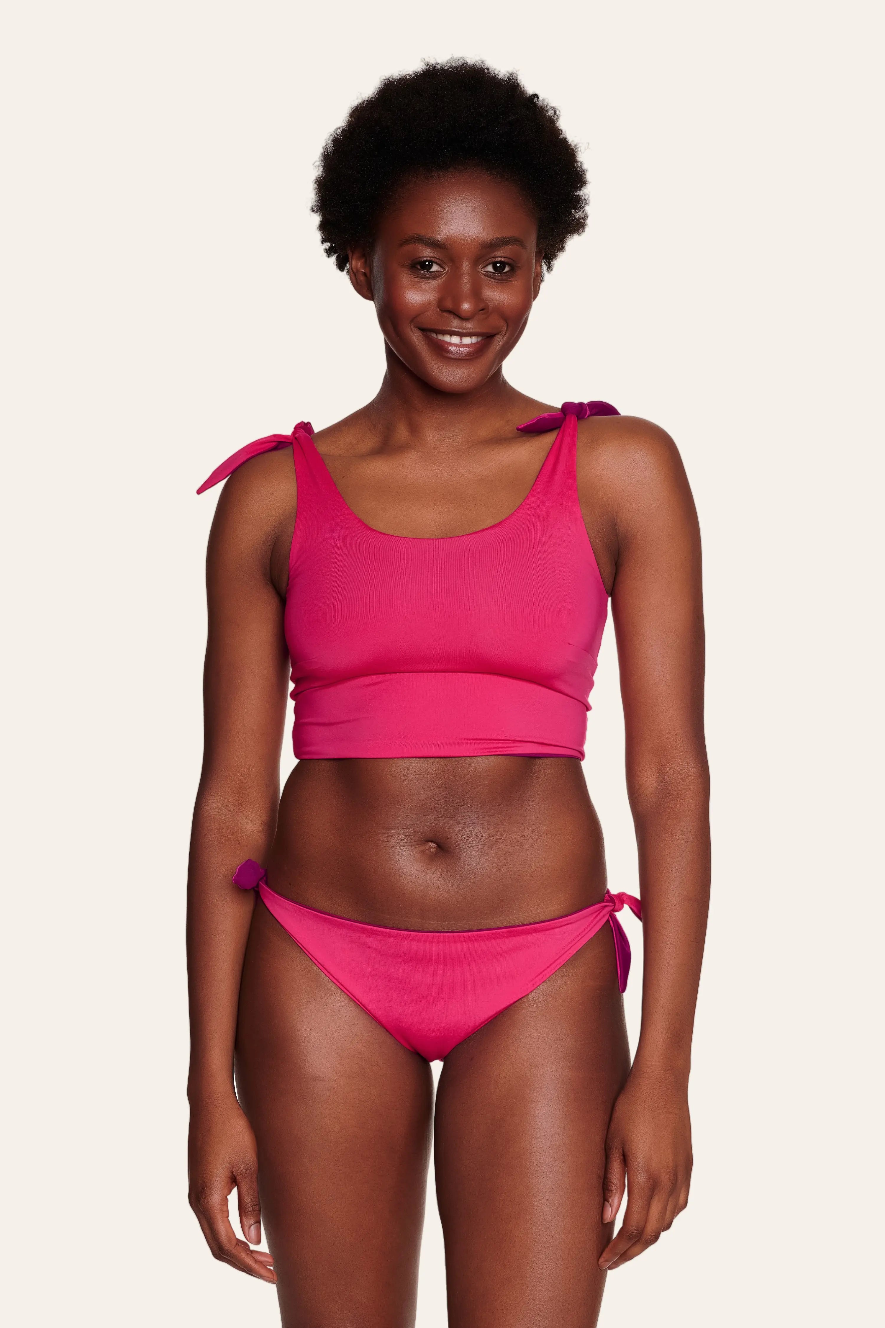 Frau trägt pinkes MYMARINI Bikinitop mit breiten Trägern und Bikinihose mit seitlichen Schleifen.#color_pink-hortensia