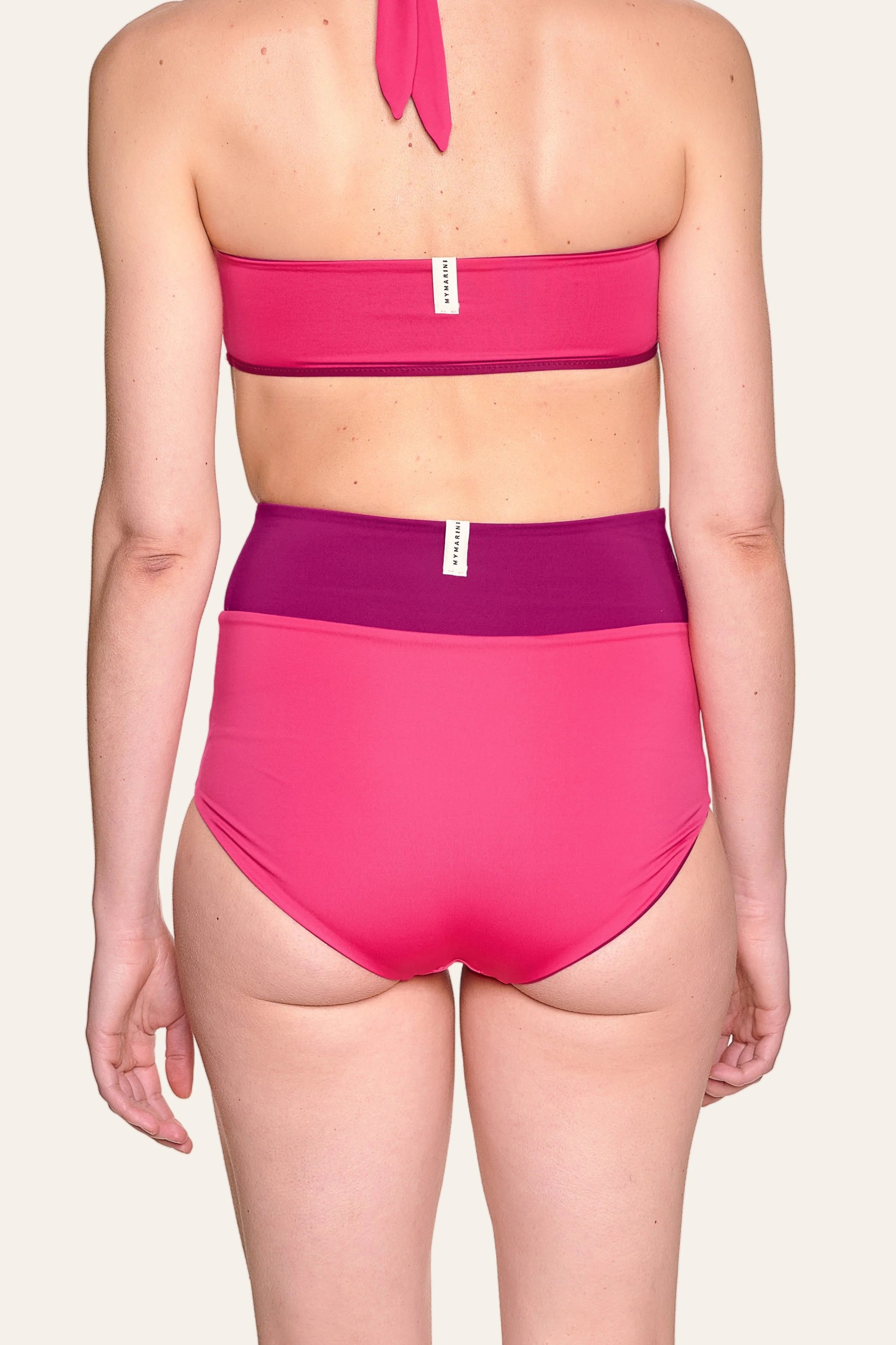 Rückansicht einer Person in einem MYMARINI Bikini mit Bandeau-Top und High-Waist-Hose in Pink und Lila.#color_pink-hortensia