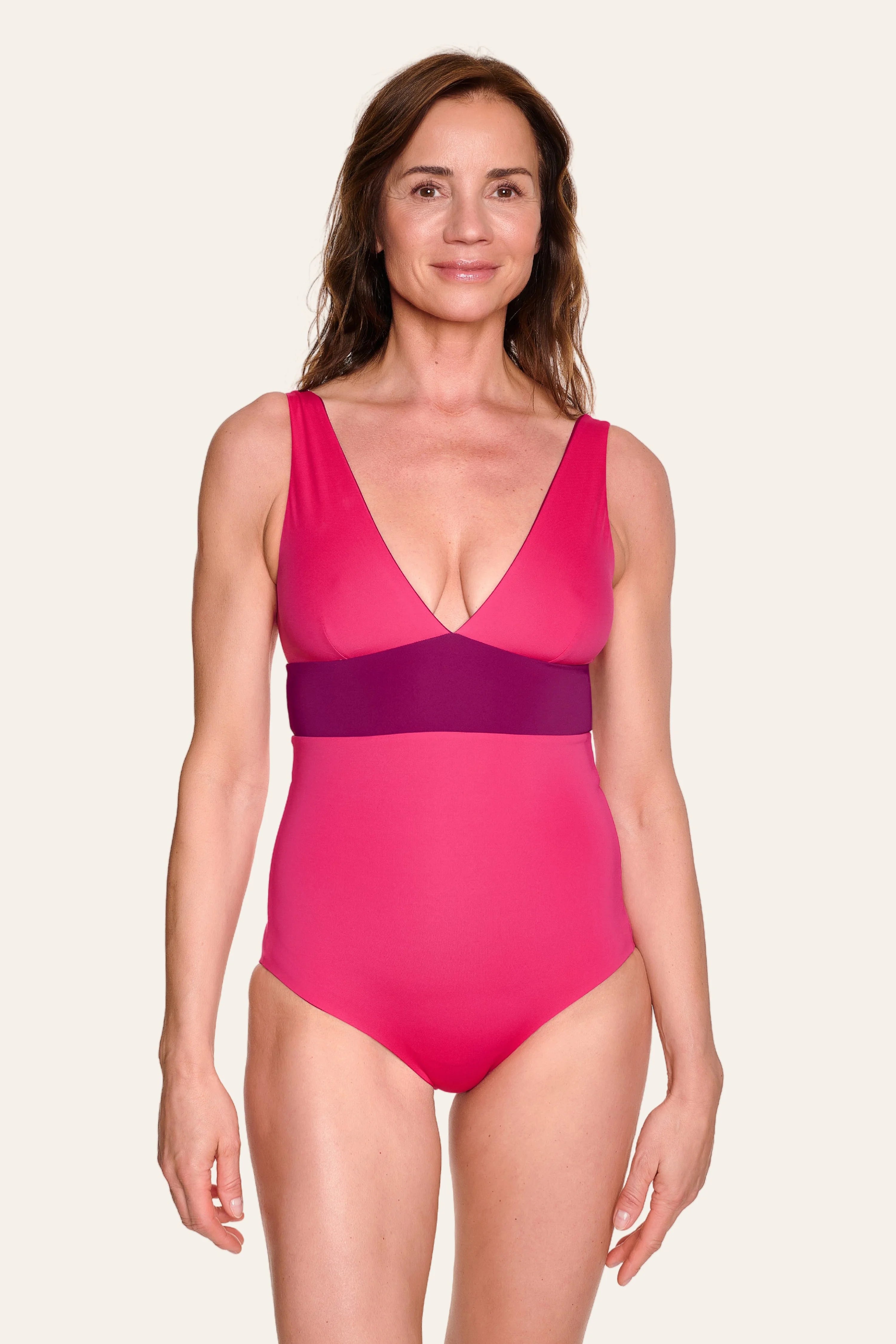 Frau trägt MYMARINI Badeanzug mit V-Ausschnitt und breiten Trägern in Pink und Lila.#color_pink-hortensia