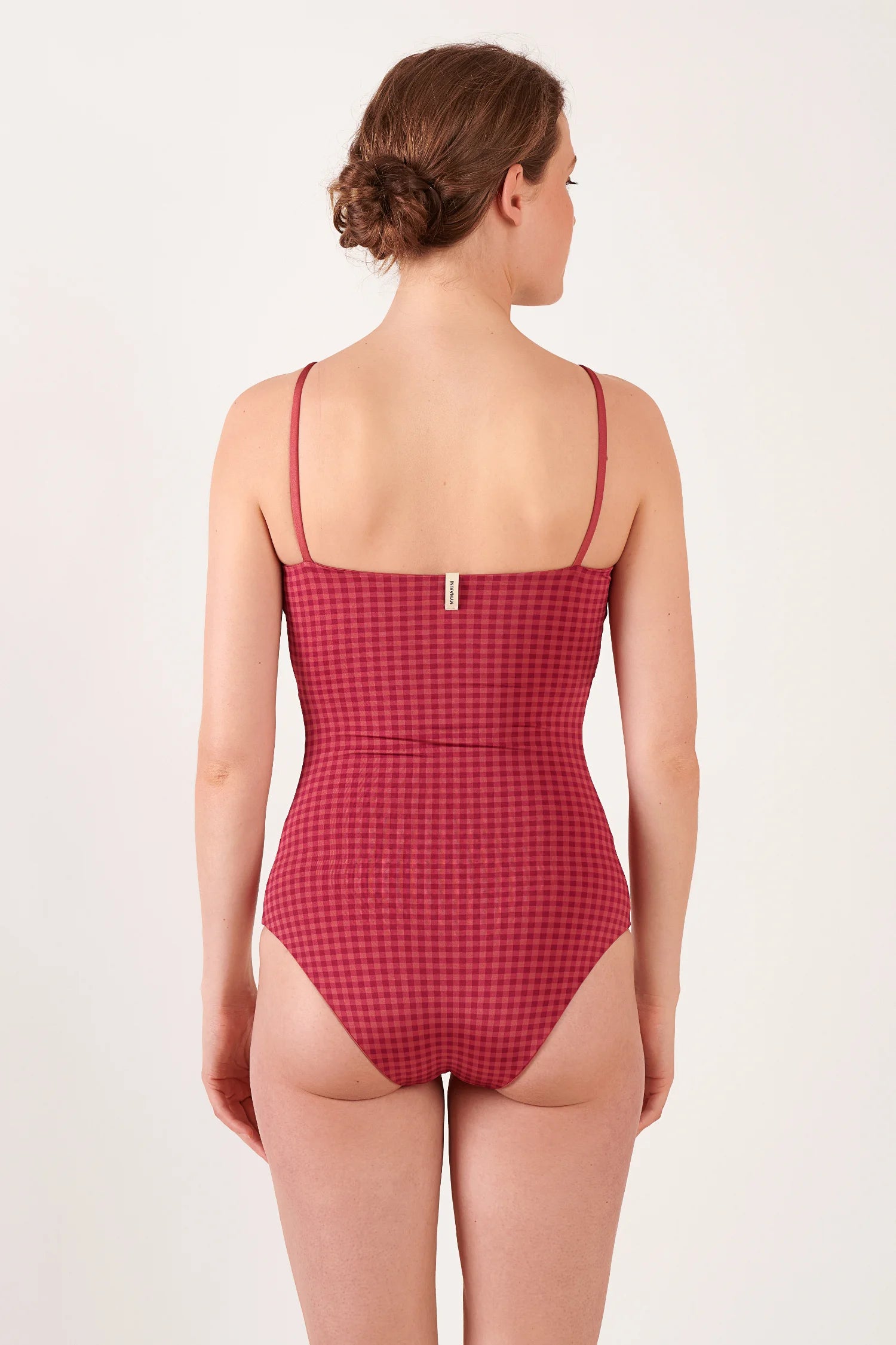 MYMARINI One-Piece mit Spaghettiträgern, hoch am Rücken, Frau posiert am Strand vor Meer.#color_rouge-vichy