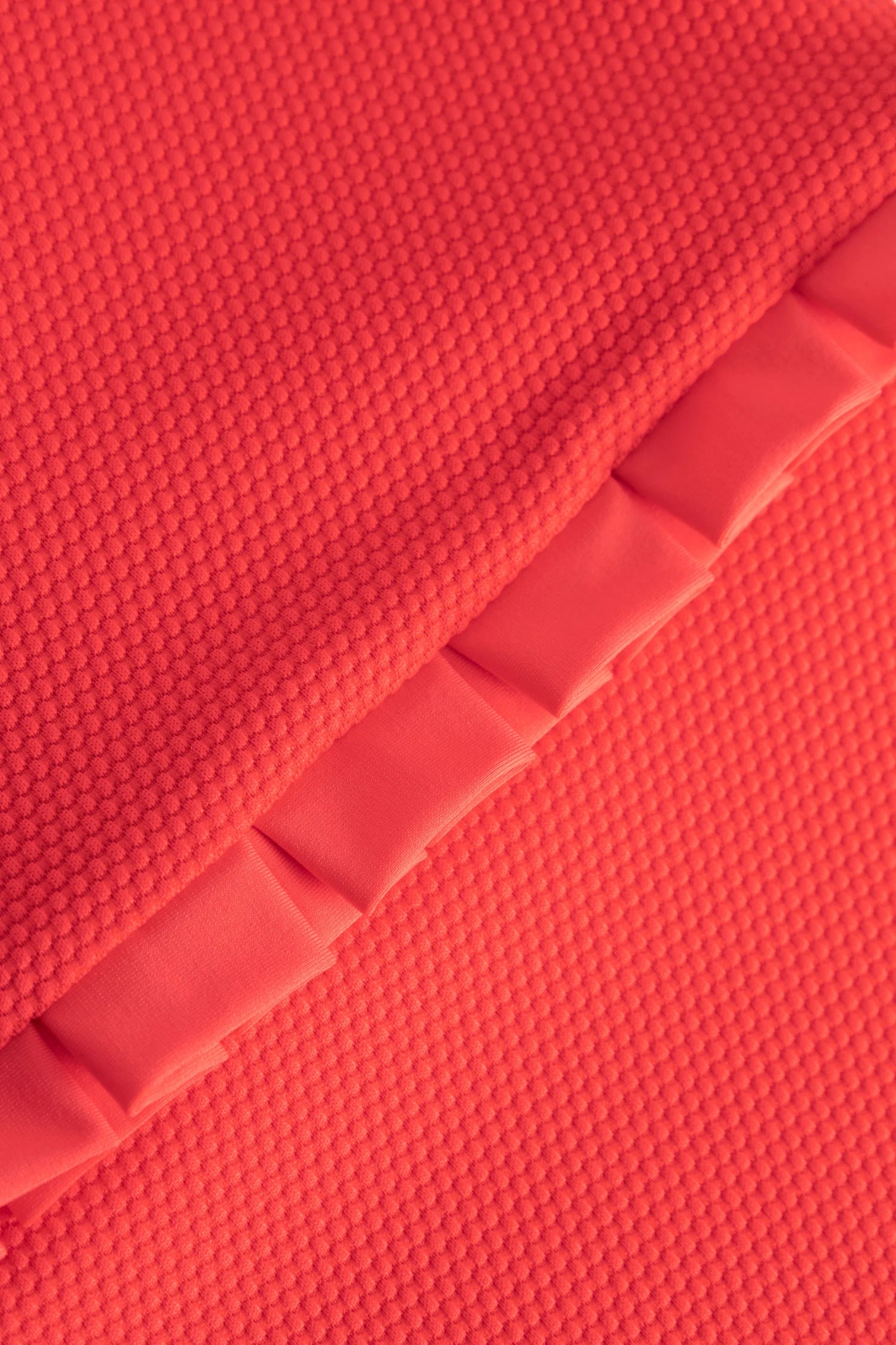 Nahaufnahme eines korallenfarbigen, strukturierten Stoffes mit einer diagonalen, glatten Falte.#color_rouge