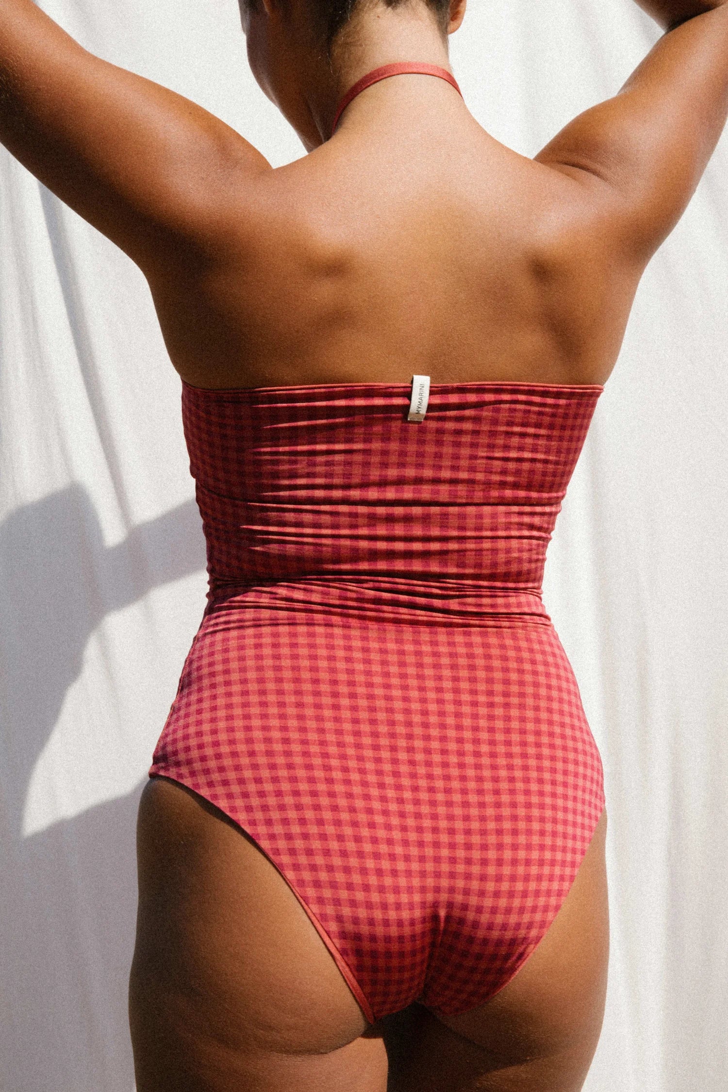 Rückenansicht der MYMARINI Bikinihose, High waist, bordeauxfarbenes Karomuster, mit sichtbarem Markenetikett.#color_rouge-vichy