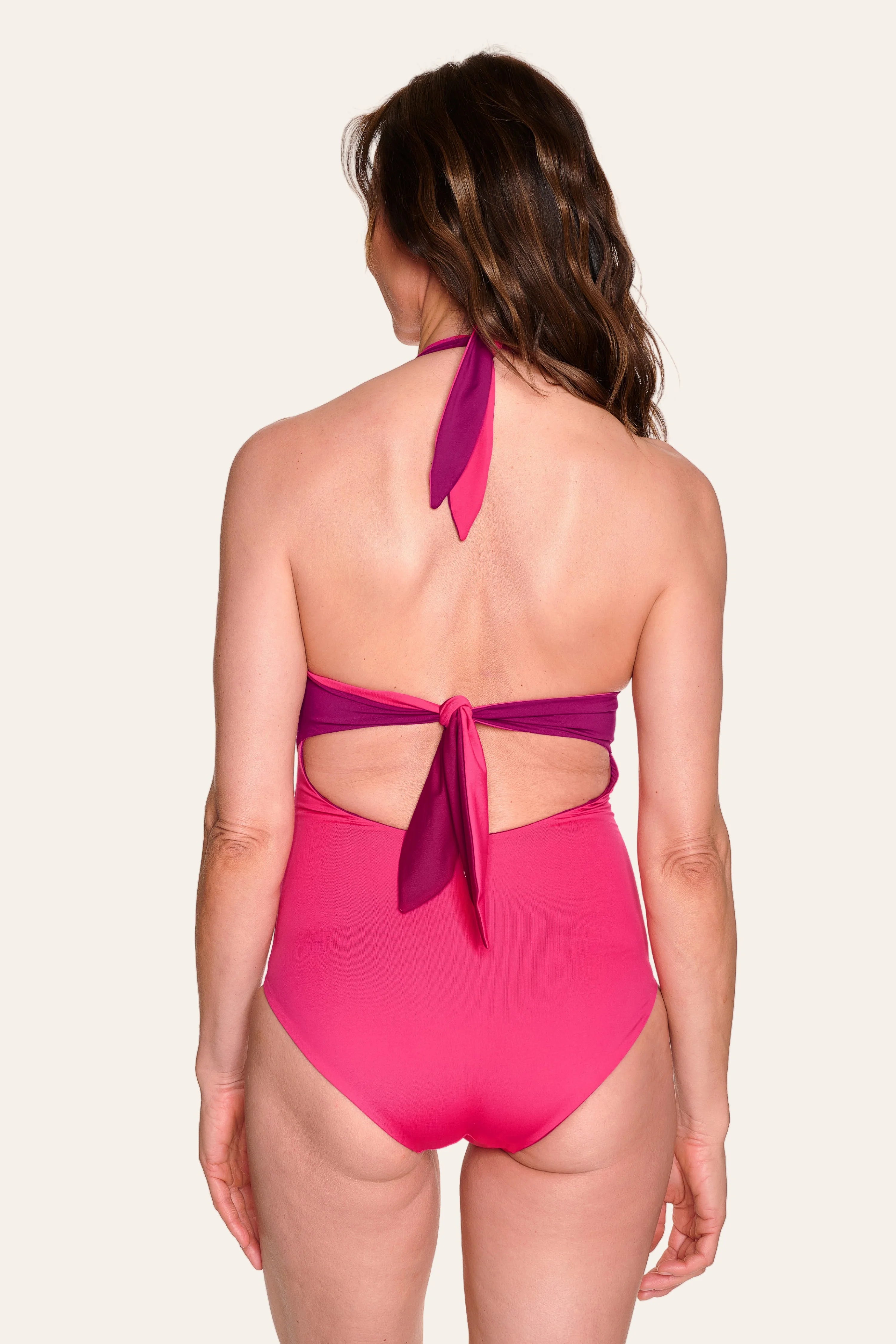 Frau in pinkem MYMARINI Neckholder-One-Piece mit tiefem Rückenausschnitt, von hinten fotografiert.#color_pink-hortensia