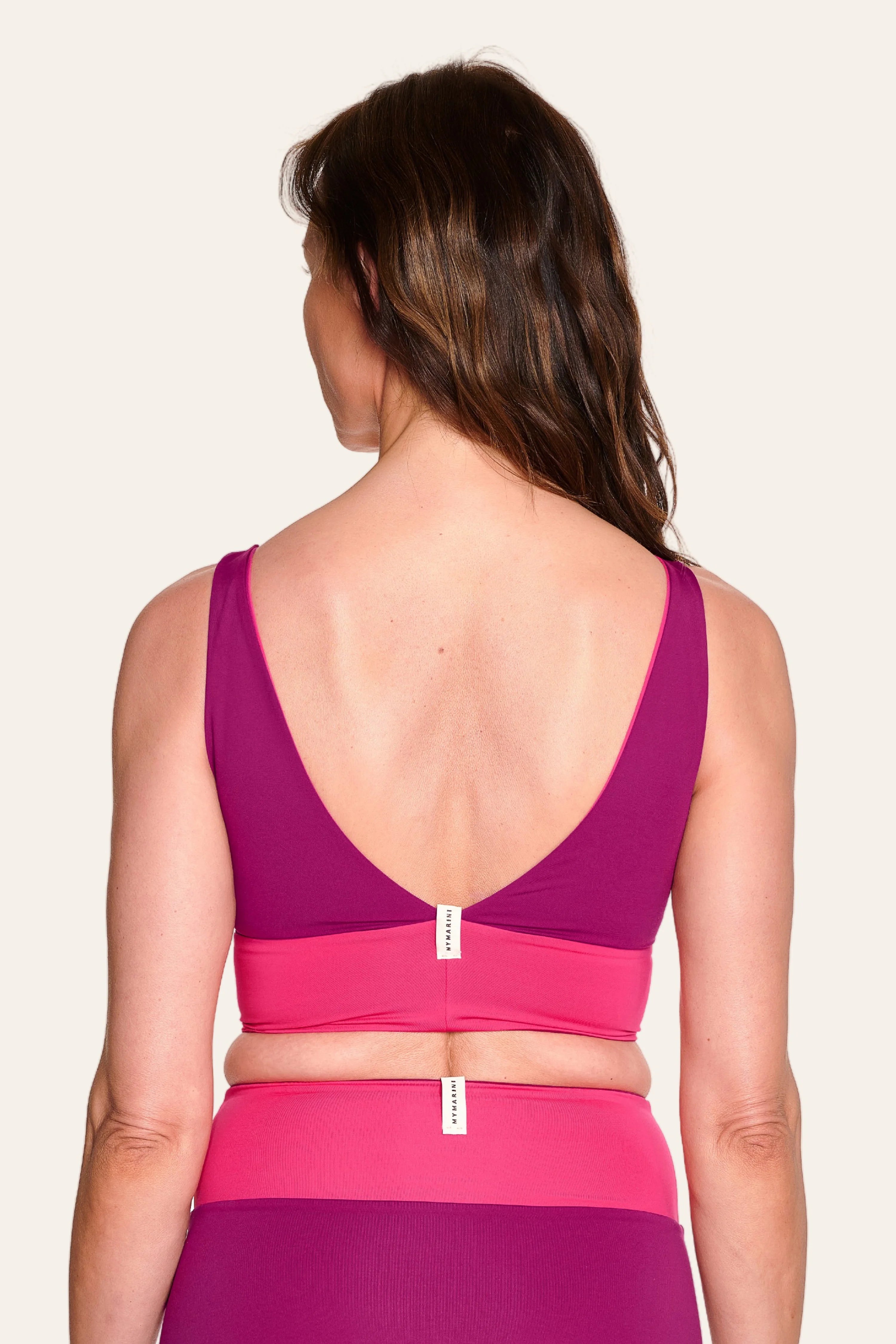 Frau in MYMARINI Bikinitop mit tiefem Rückenausschnitt und Bikinihose in Pink und Lila, von hinten gezeigt.#color_pink-hortensia