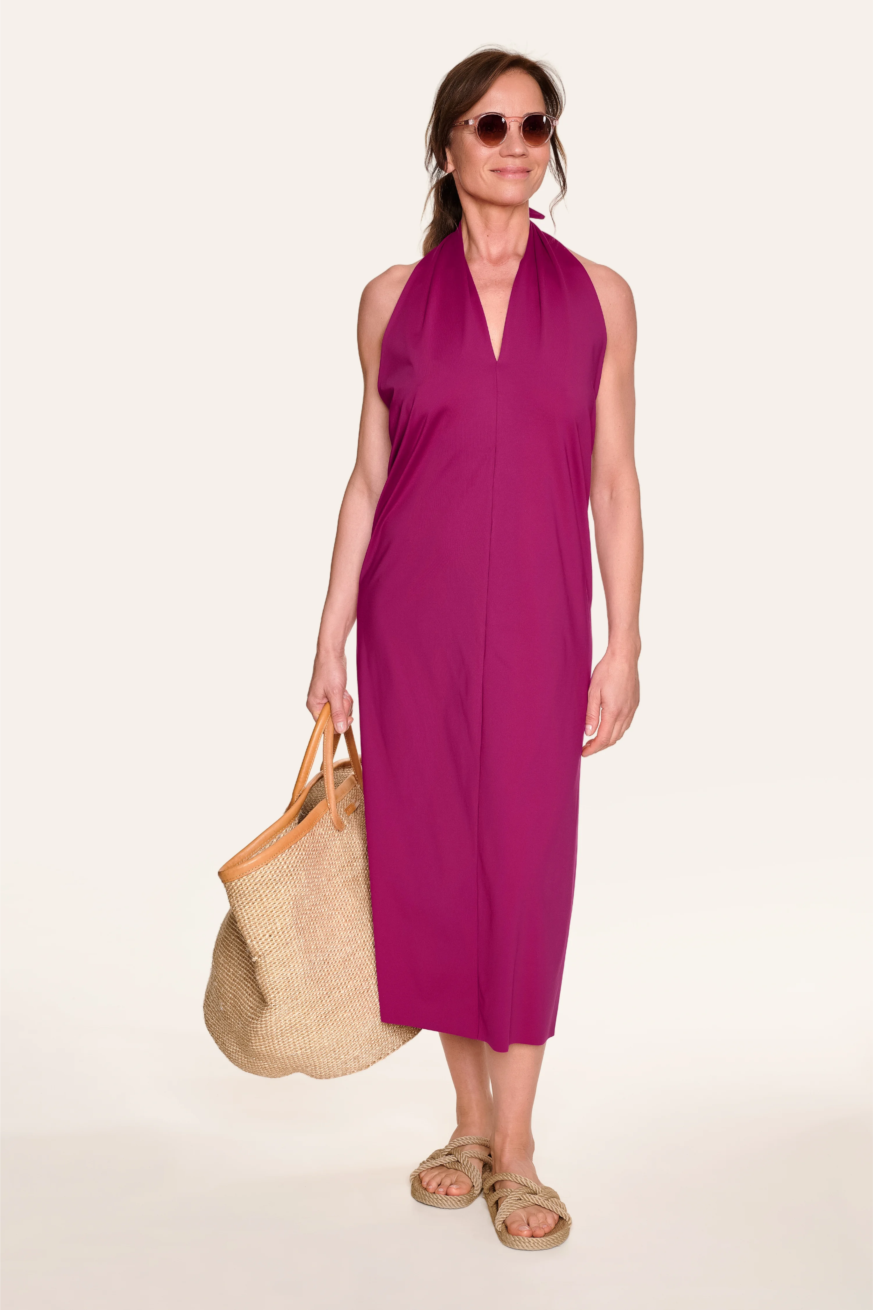 Frau in lila MYMARINI-Kleid mit Neckholder-Schnitt, trägt Sonnenbrille und Strohtasche.#color_hortensia