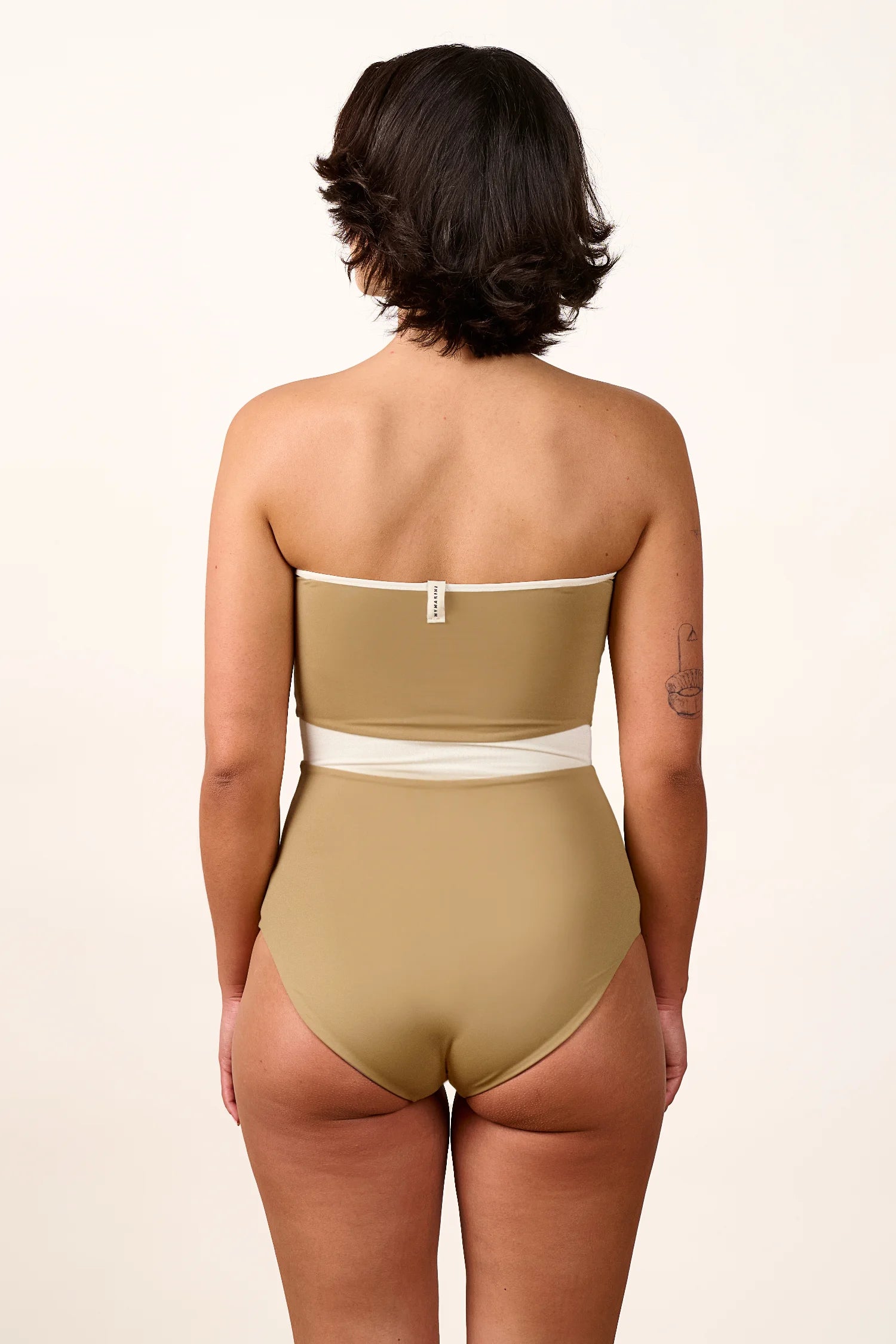 Person von hinten in einem MYMARINI Bandeau-One-Piece mit hohem Beinausschnitt in Beige und Weiß.#color_coast-desert