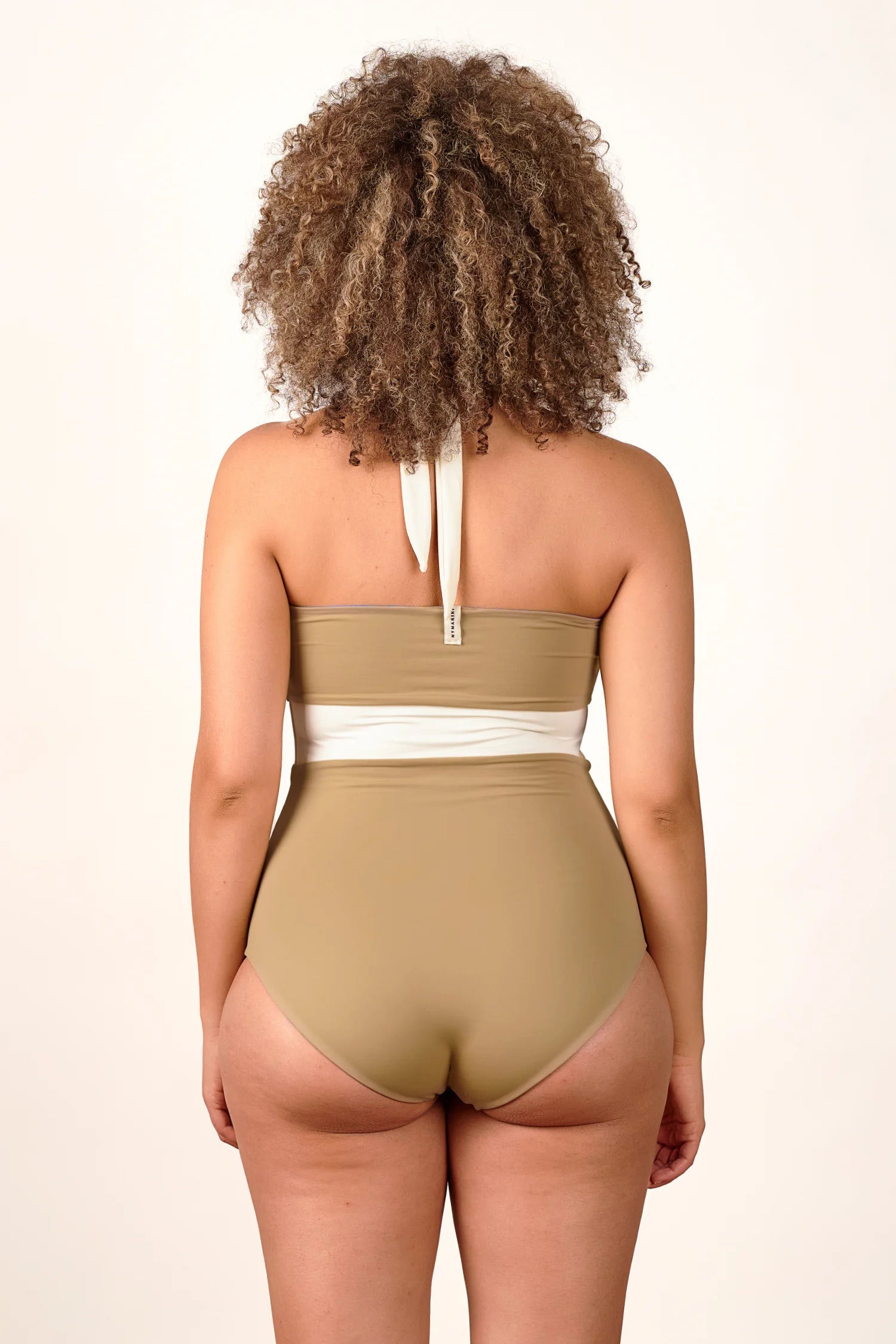 Person von hinten in einem MYMARINI Neckholder-One-Piece mit hohem Beinausschnitt in Beige und Weiß.#color_coast-desert