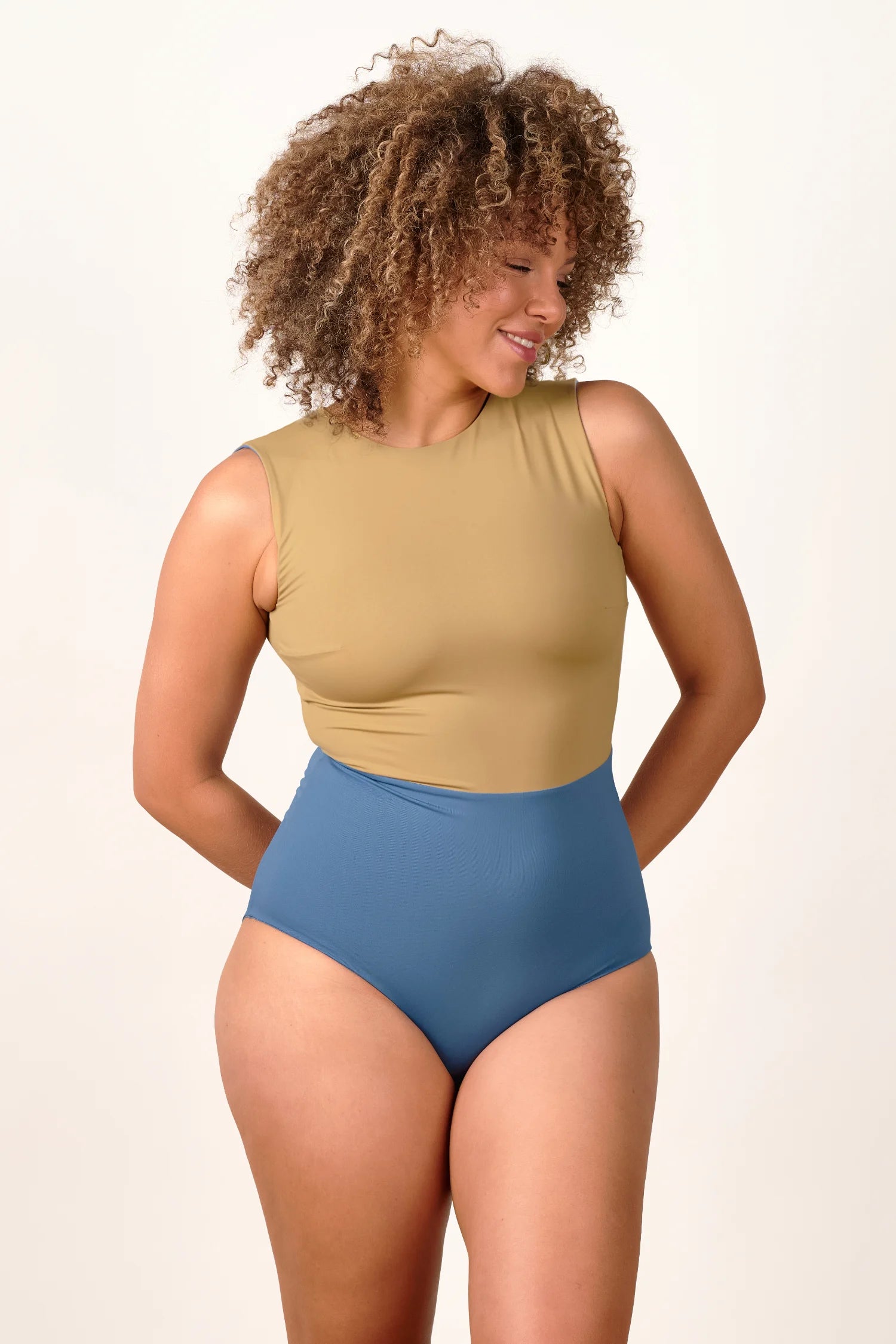 Frau trägt MYMARINI One-Piece Badeanzug in Beige und Blau, hoch geschlossen, mit breiten Trägern.#color_coast-desert