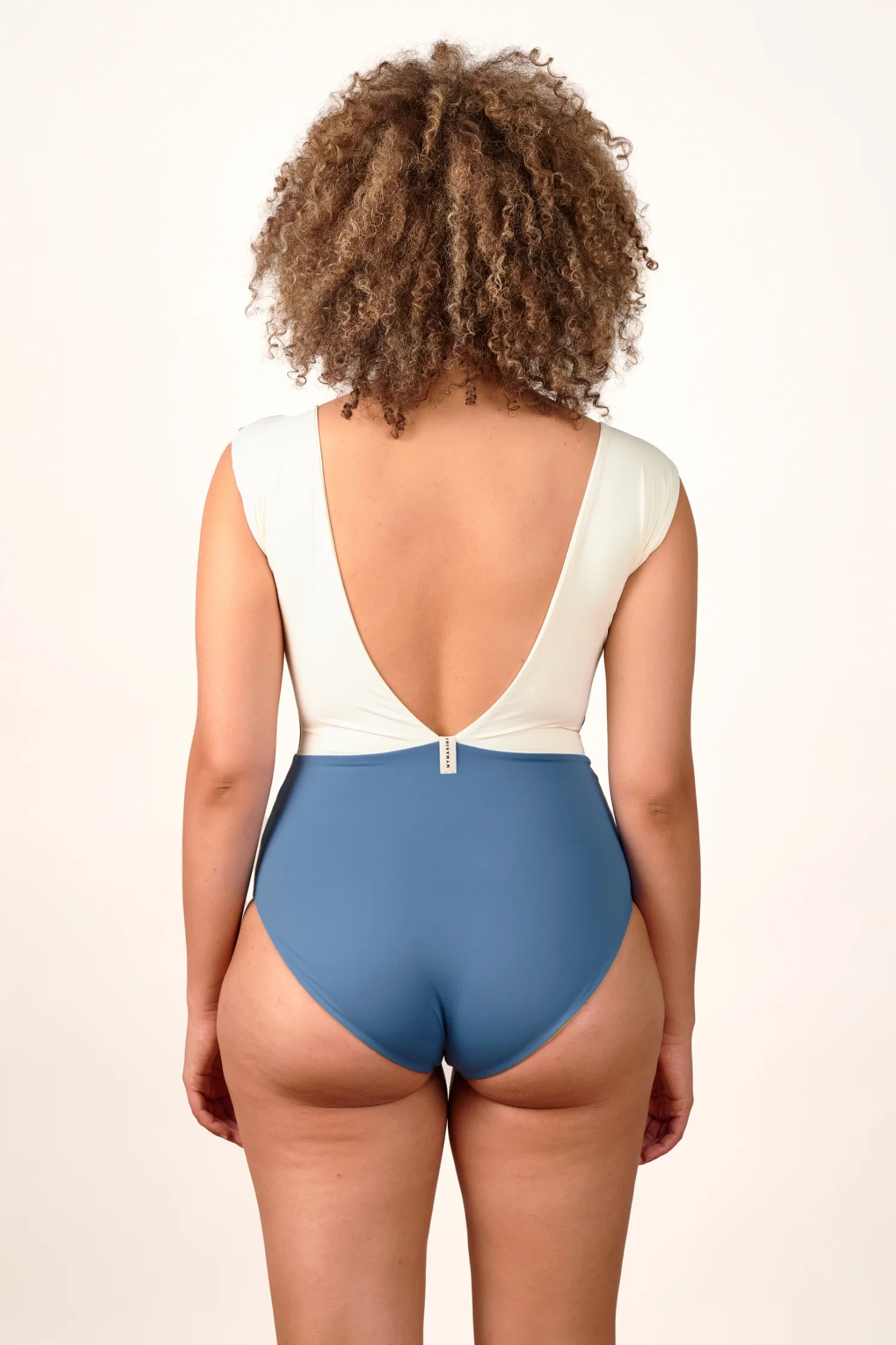 Person trägt einen MYMARINI Badeanzug mit tiefem Rückenausschnitt und hohem Beinausschnitt in Weiß und Blau.#color_coast-desert