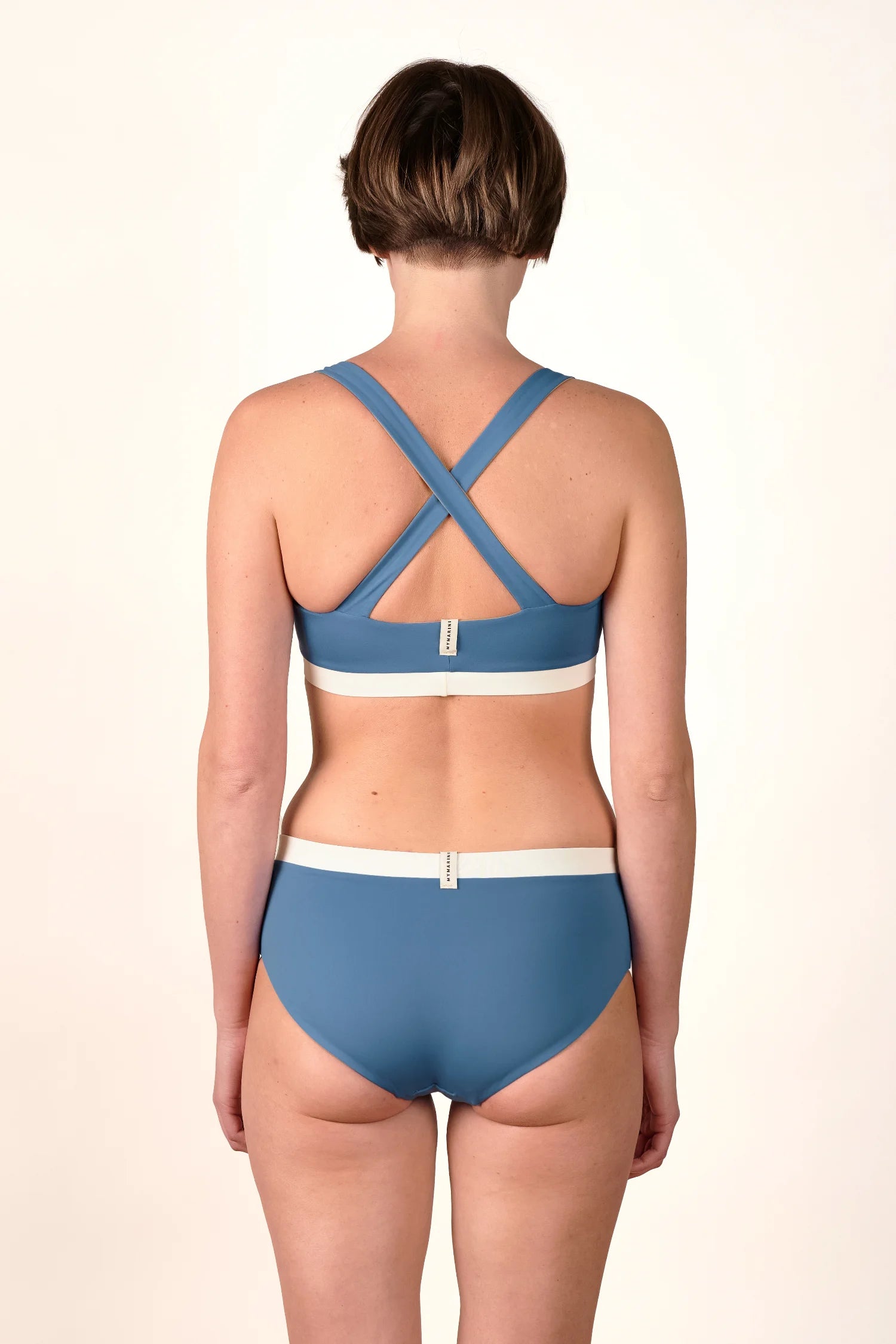 Frau in MYMARINI Bikini mit Cross Top und High Waist Hose in Blau, Rückansicht.#color_coast-desert