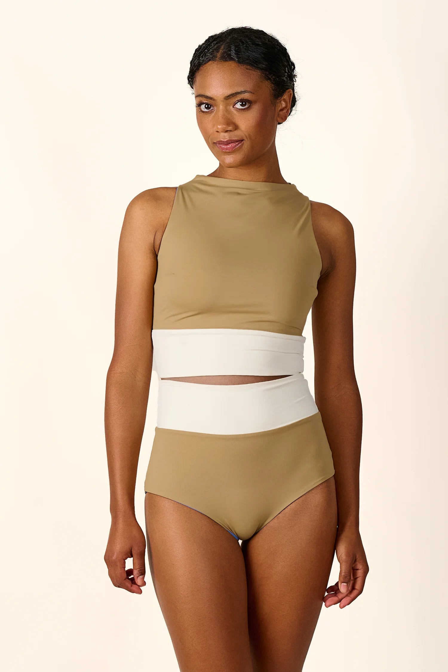 Frau trägt MYMARINI Badeanzug mit hoch geschlossenem Schnitt und hohem Beinausschnitt in Beige und Weiß.#color_coast-desert