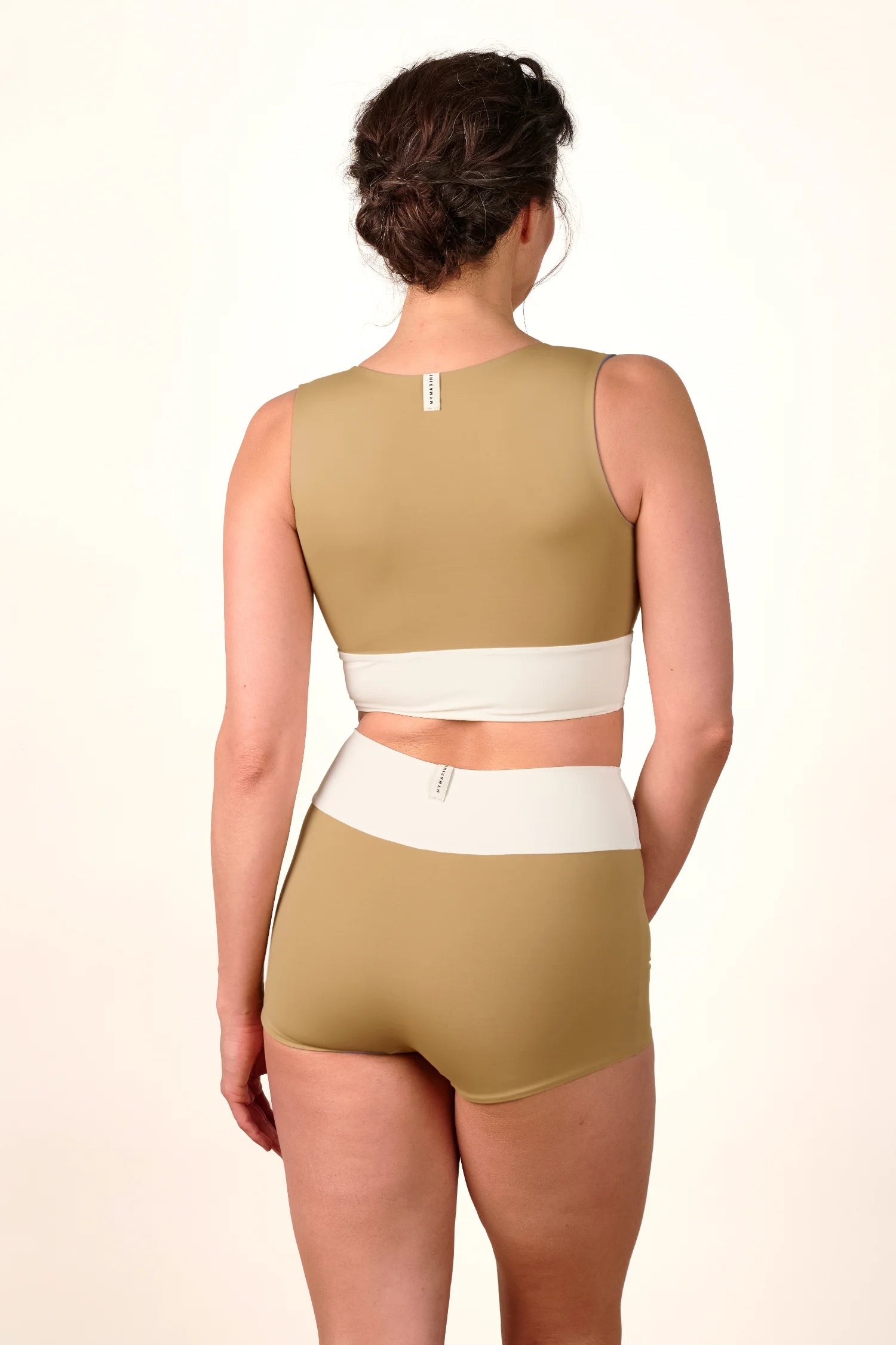 Frau in MYMARINI Bikinihose und Top, hoch geschlossen, breiter Träger, in Beige und Weiß, von hinten.#color_coast-desert