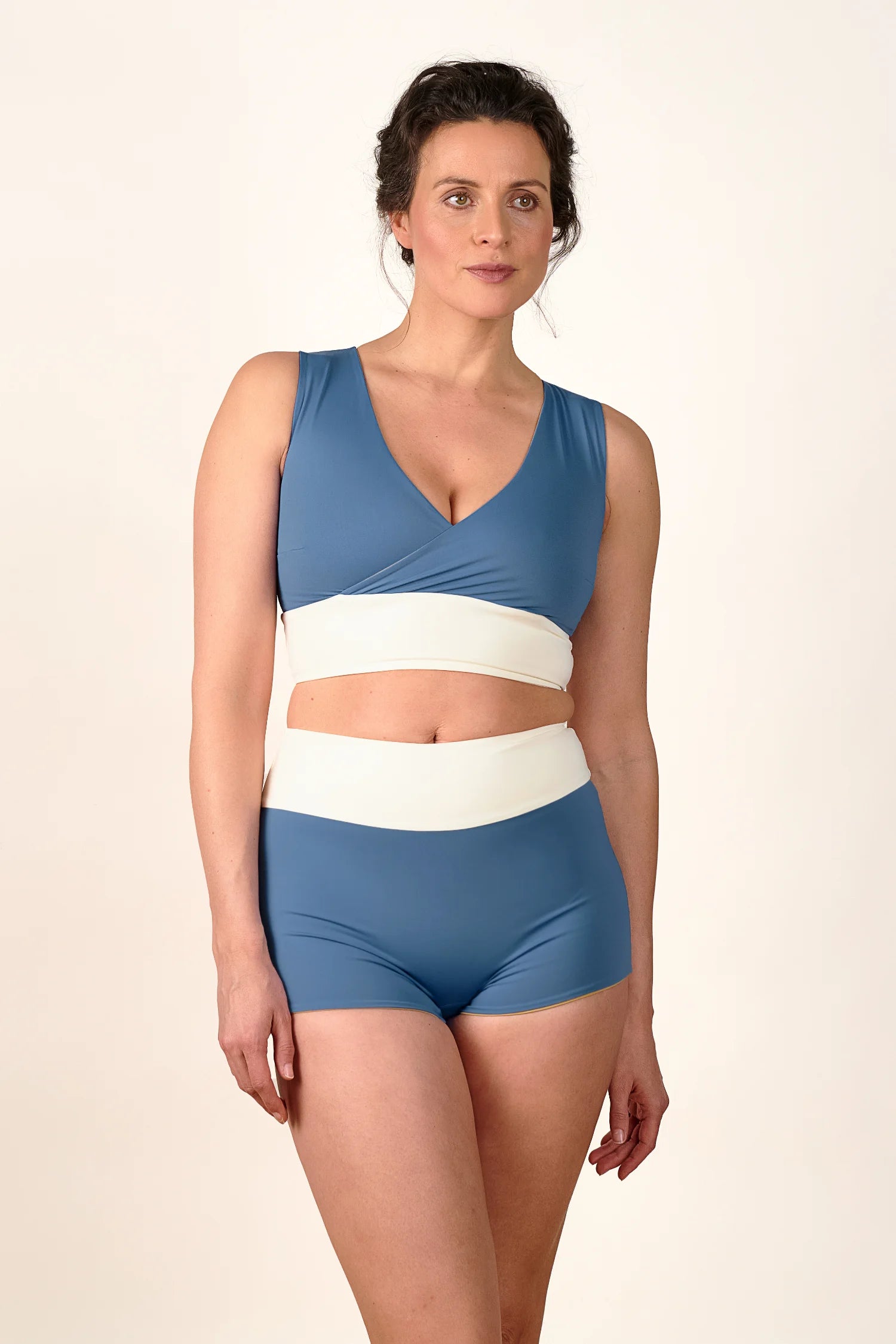 Frau trägt MYMARINI Bikinitop mit V-Ausschnitt und Bikinihose in High Waist, beide in Blau und Weiß.#color_coast-desert