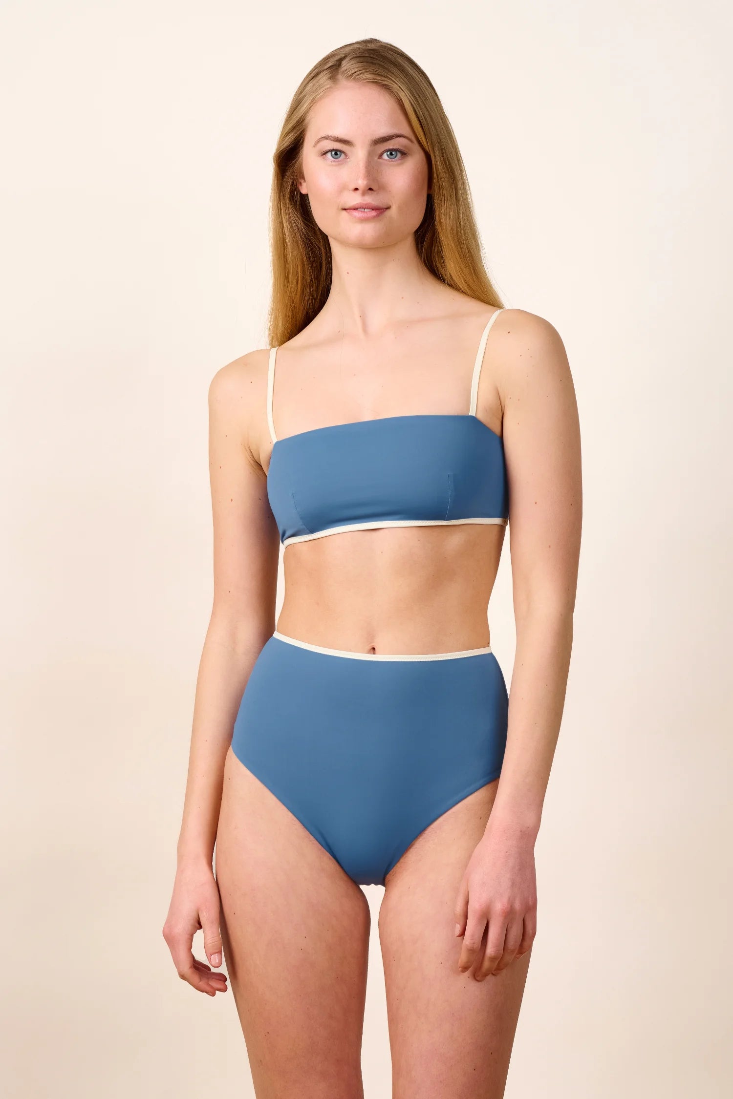 Frau trägt MYMARINI Bikini mit Bandeau-Top und High-Waist-Hose in Blau mit weißen Details.#color_coast-desert