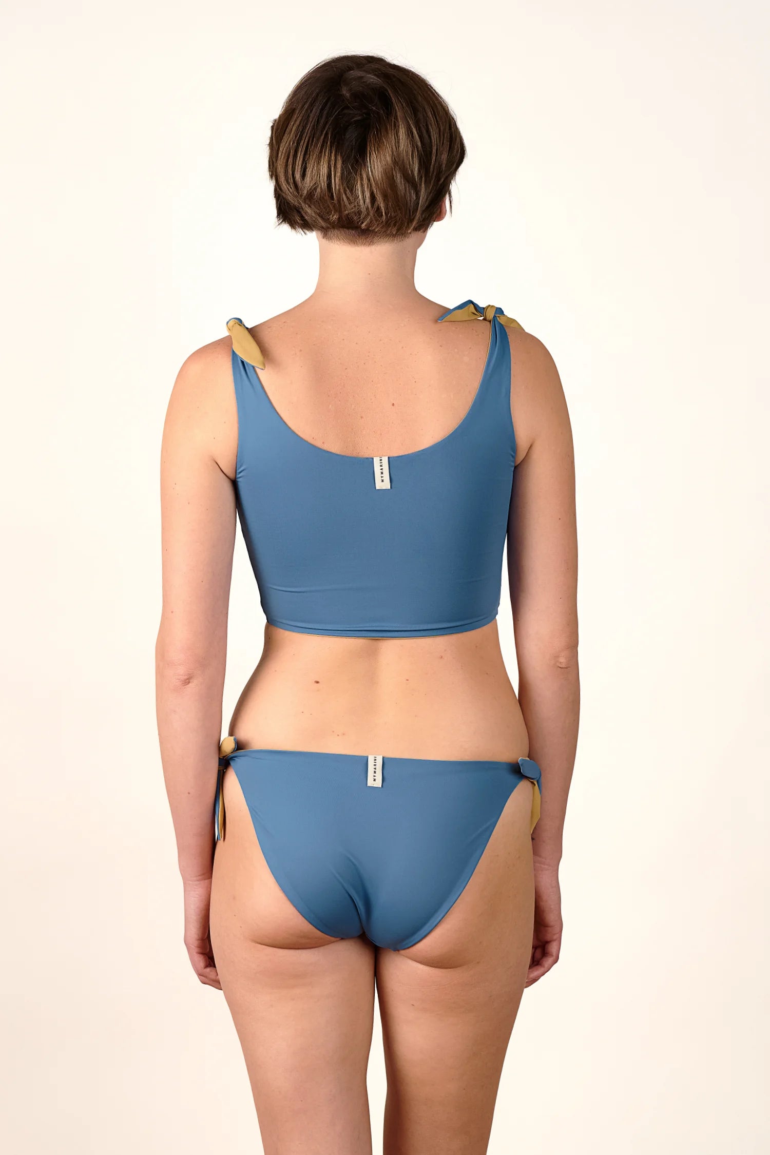 Rückansicht einer Frau in einem MYMARINI Bikini mit breiten Trägern und hohem Beinausschnitt, in Blau.#color_coast-desert