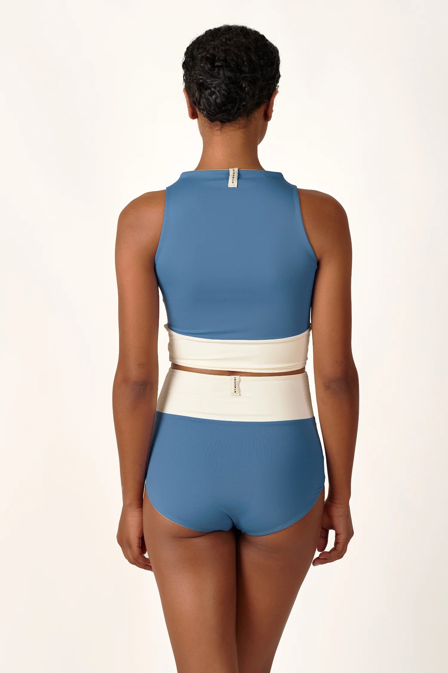 Rückansicht einer Person in einem MYMARINI Bikini mit hochgeschlossenem Top und Mid-Rise-Hose in Blau und Weiß.#color_coast-desert