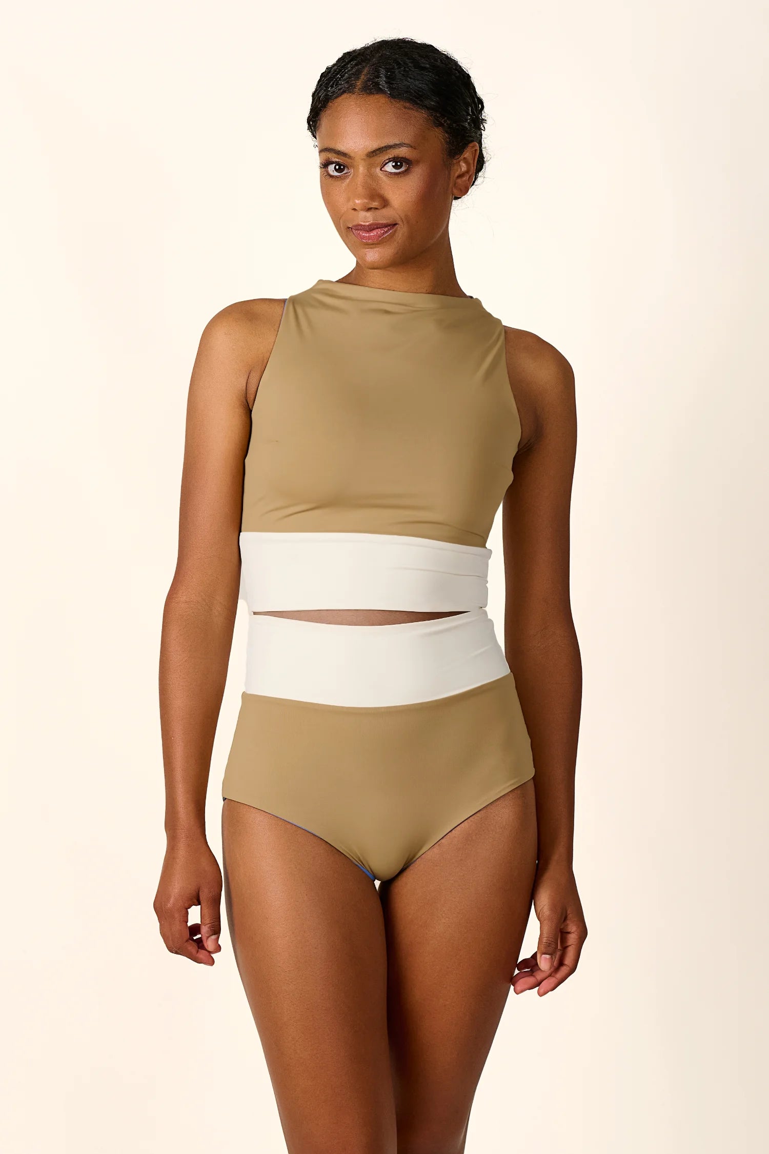 Frau trägt MYMARINI Badeanzug mit hochgeschlossenem Schnitt und hohem Beinausschnitt in Beige und Weiß.#color_coast-desert