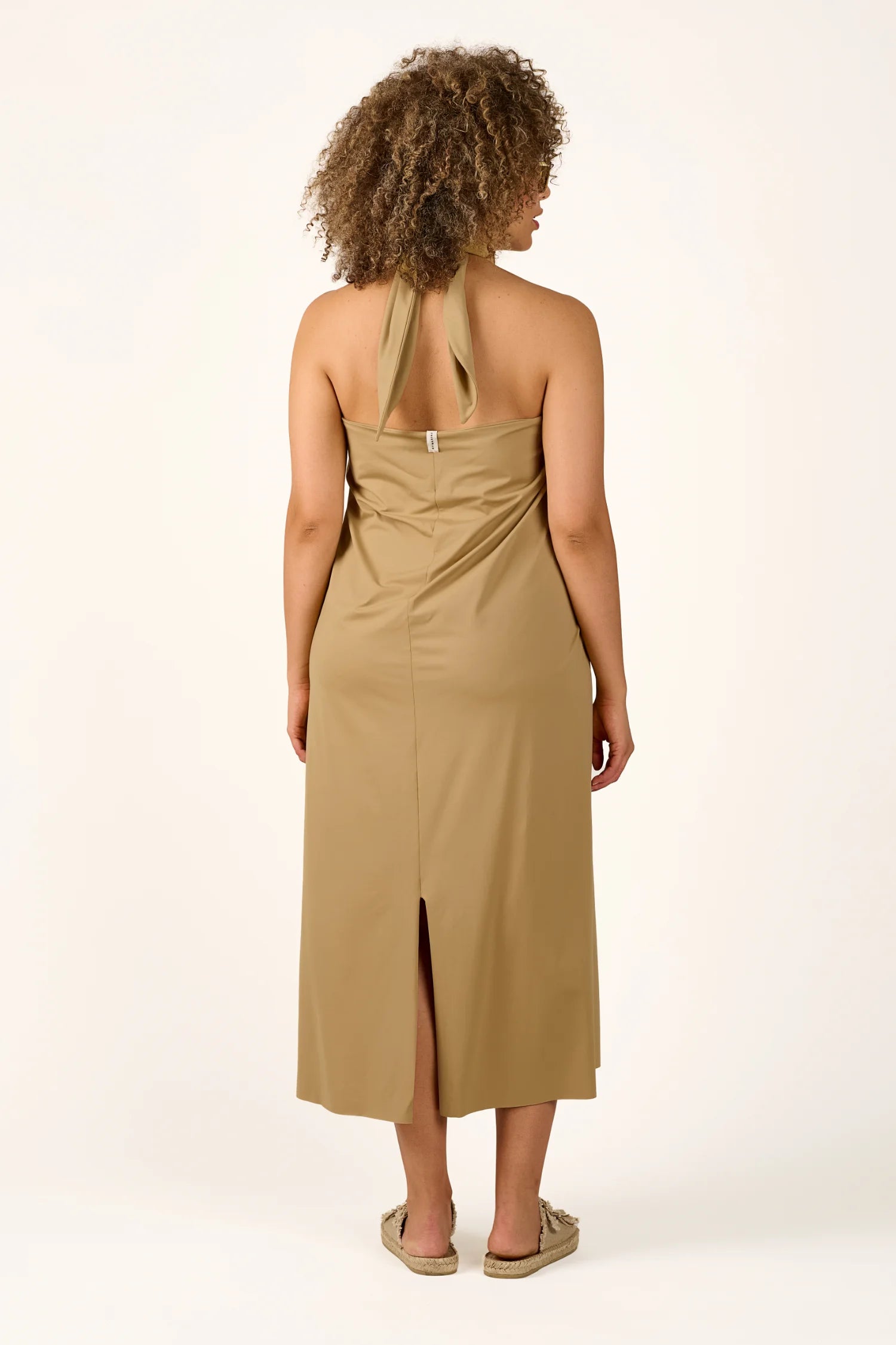 Person von hinten in einem MYMARINI Neckholder-Kleid in Beige, knielang mit Rückenschlitz.#color_desert