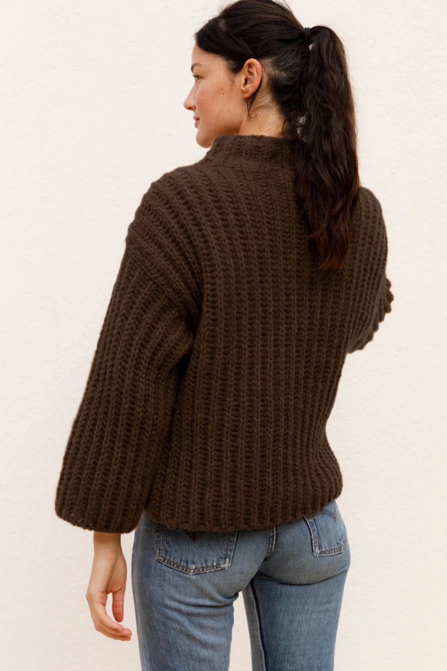 Frau in braunem Strickpullover und blauer Jeans von hinten, MYMARINI.#color_chocolate