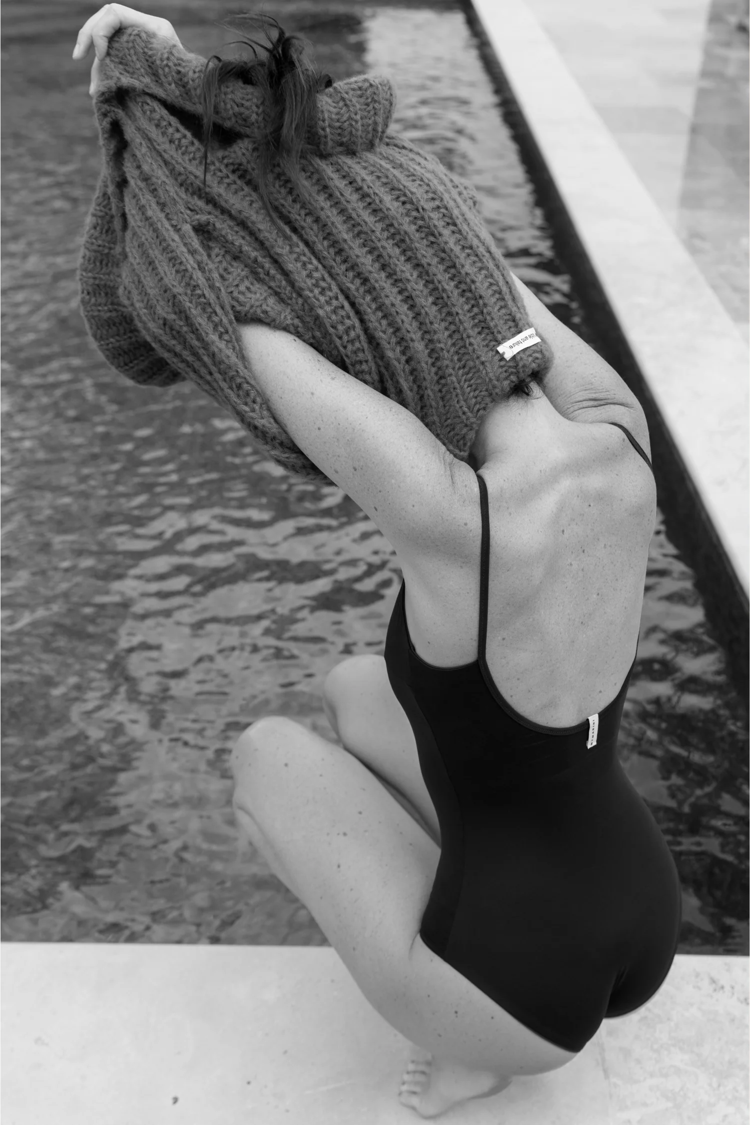 Person in einem schwarzen Badeanzug, die eine Strickmütze am Pool hält.#color_chocolate