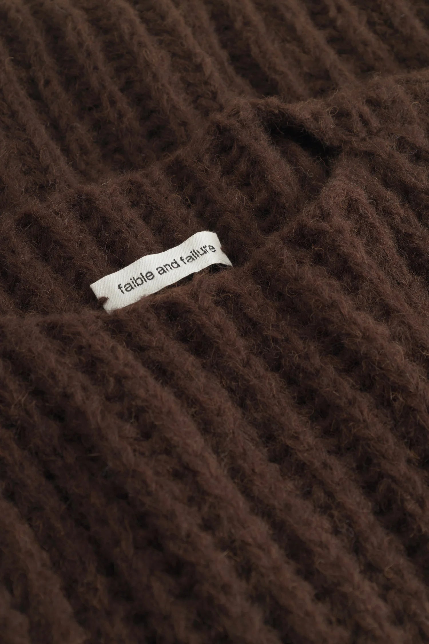 Brauner Strickstoff mit einem kleinen weißen Etikett, auf dem "fable and failure" steht.#color_chocolate