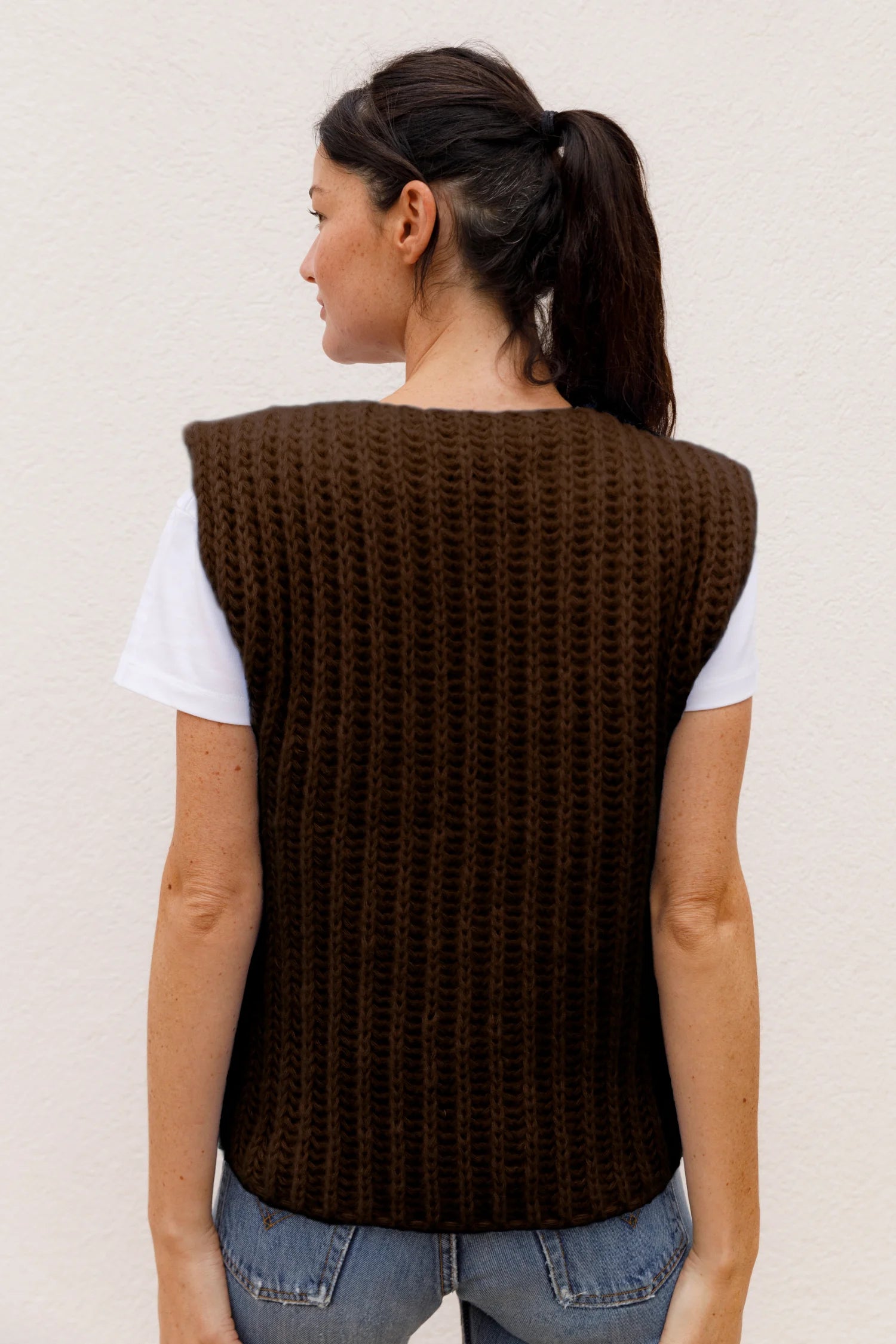 Frau von hinten in braunem MYMARINI-Top mit breiten Trägern über weißem T-Shirt, trägt Jeans.#color_chocolate