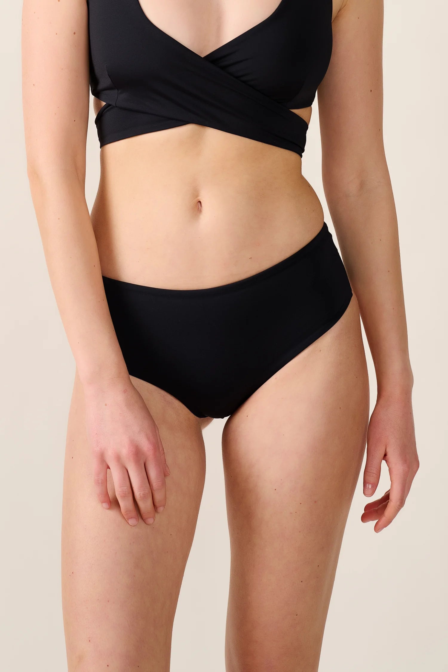 Schwarze MYMARINI Bikinihose, hoher Beinausschnitt, kombiniert mit schwarzem Cross Top.#color_black-navy