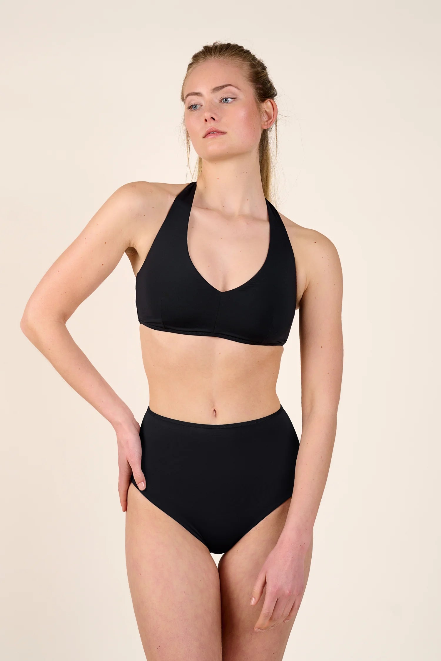 Frau trägt schwarzen MYMARINI Bikini mit Neckholder-Top und High-Waist-Hose vor neutralem Hintergrund.#color_black-navy