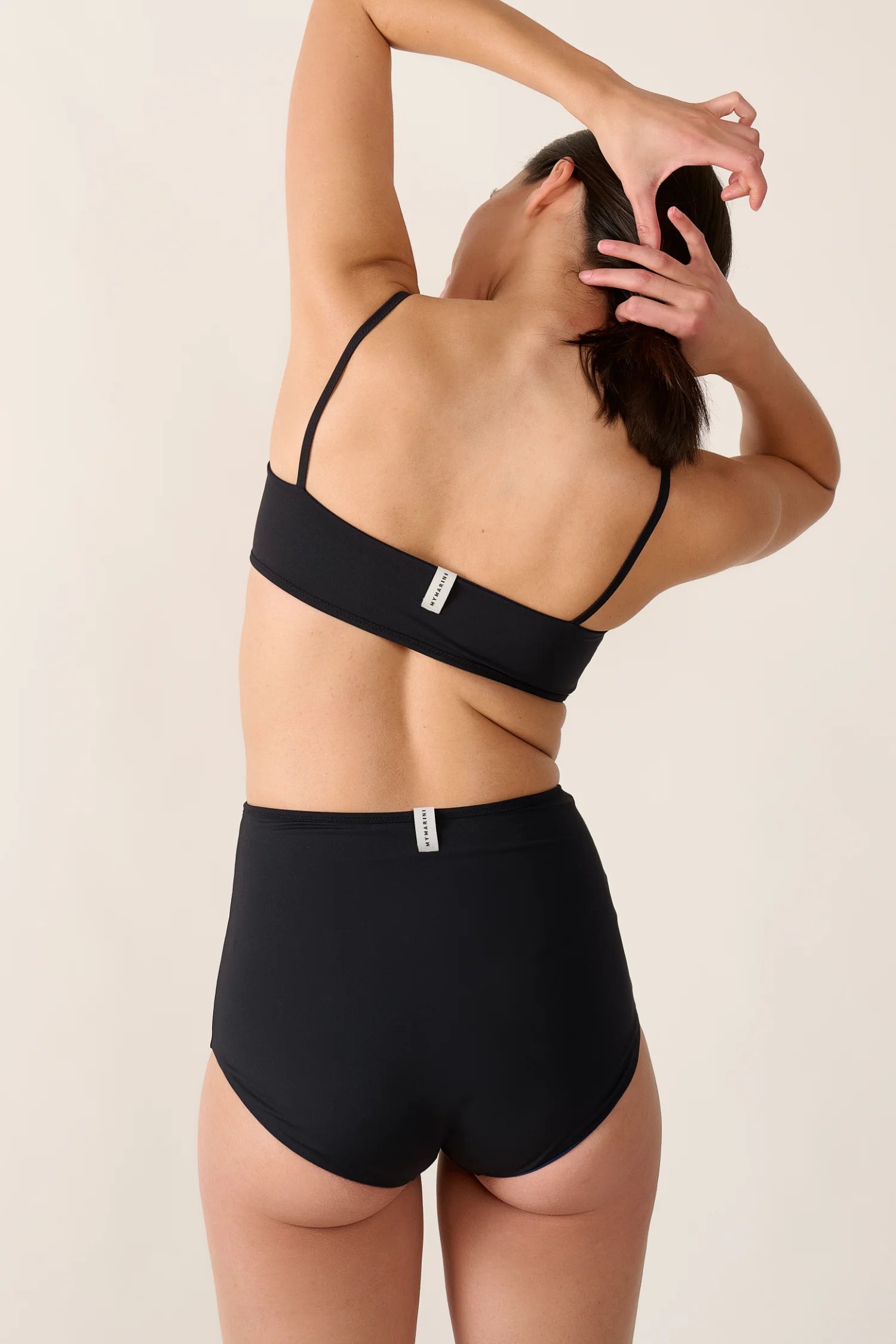 Rückansicht einer Person in schwarzem MYMARINI Bikinitop mit Spaghettiträgern und High-Waist-Bikinihose.#color_black-navy