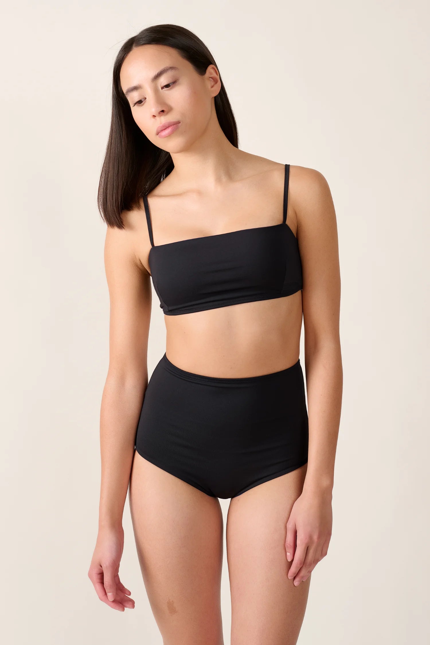 Frau trägt MYMARINI Bikinitop mit Spaghettiträgern und High-Waist-Bikinihose in Schwarz.#color_black-navy