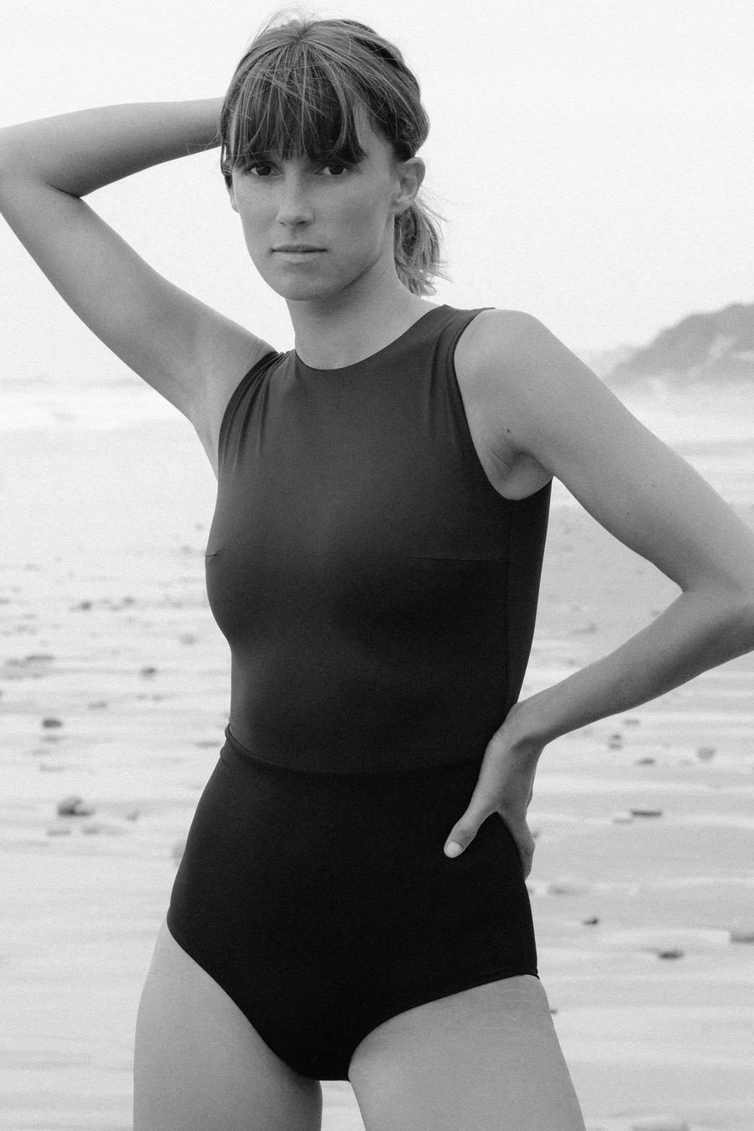 Frau am Strand in einem hoch geschlossenen MYMARINI Badeanzug mit breiten Trägern in Blau und Schwarz.#color_black-navy