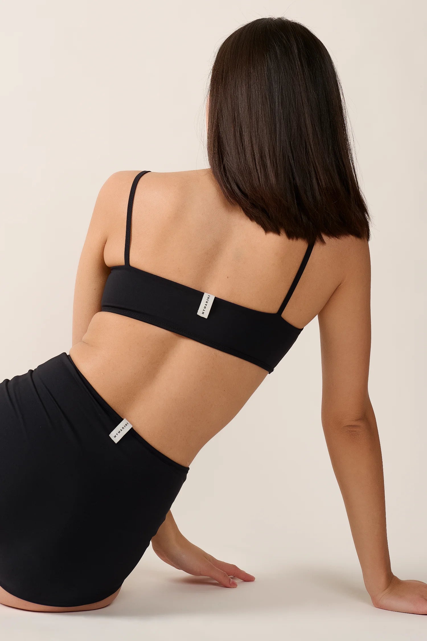 Rückansicht einer Person in MYMARINI Bademode: Schwarzes Bikinitop mit Spaghettiträgern und High-Waist-Bikinihose.#color_black-navy