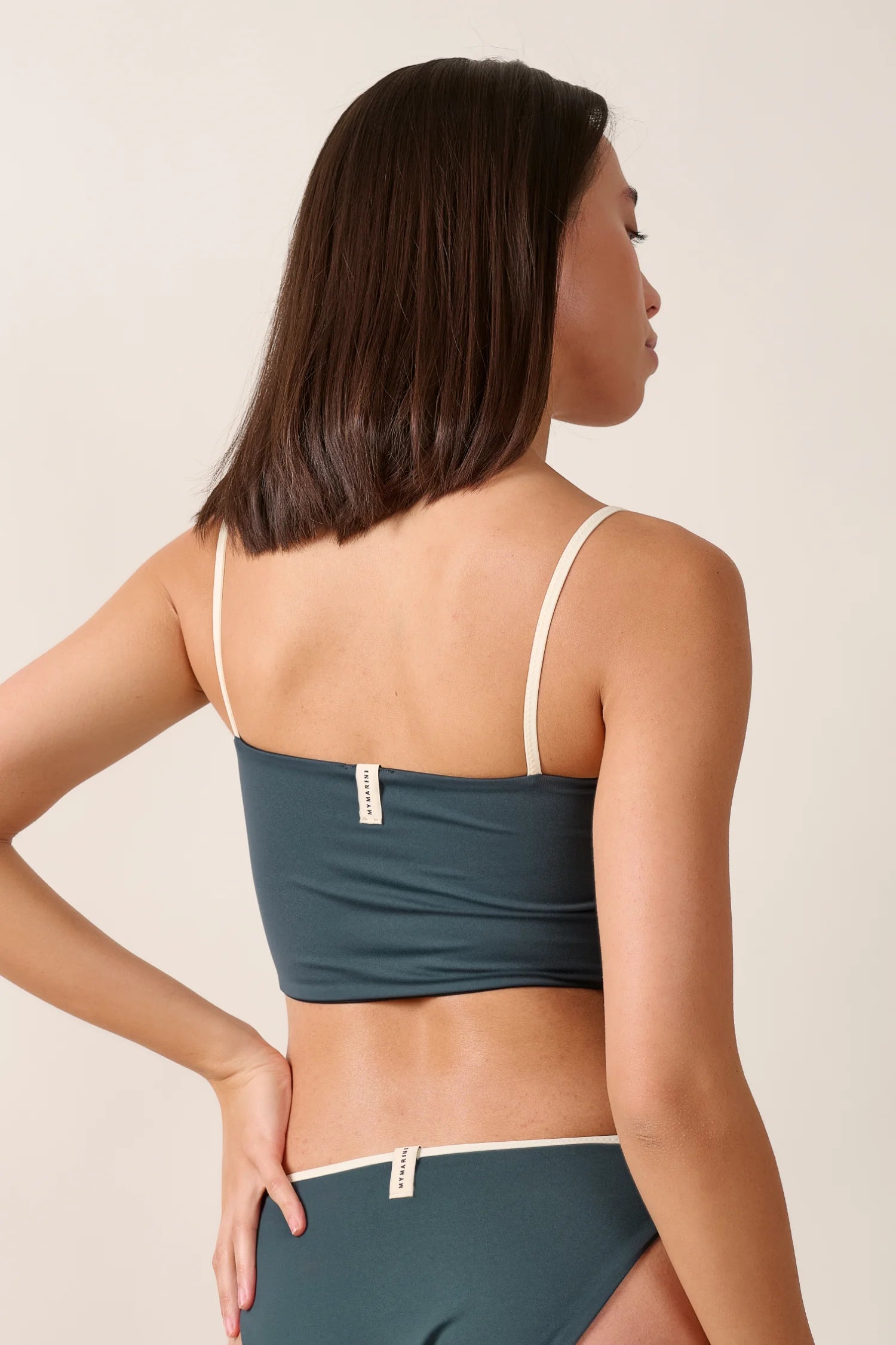 Frau trägt MYMARINI Bikinitop mit Spaghettiträgern und Bikinihose, beide in dunklem Ton mit hellem Rand.#color_black-grey-white