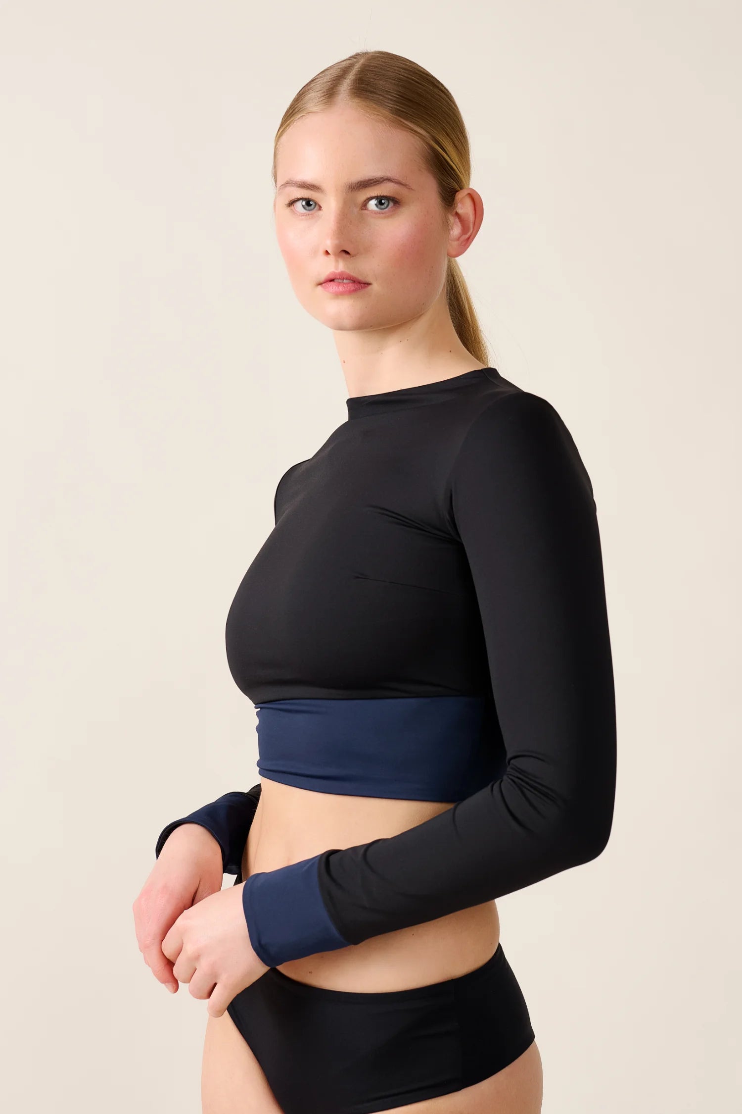 Frau trägt MYMARINI Langarm-Bikinitop mit hochgeschlossenem Schnitt in Schwarz und Blau, kombiniert mit schwarzer Bikinihose.#color_black-navy