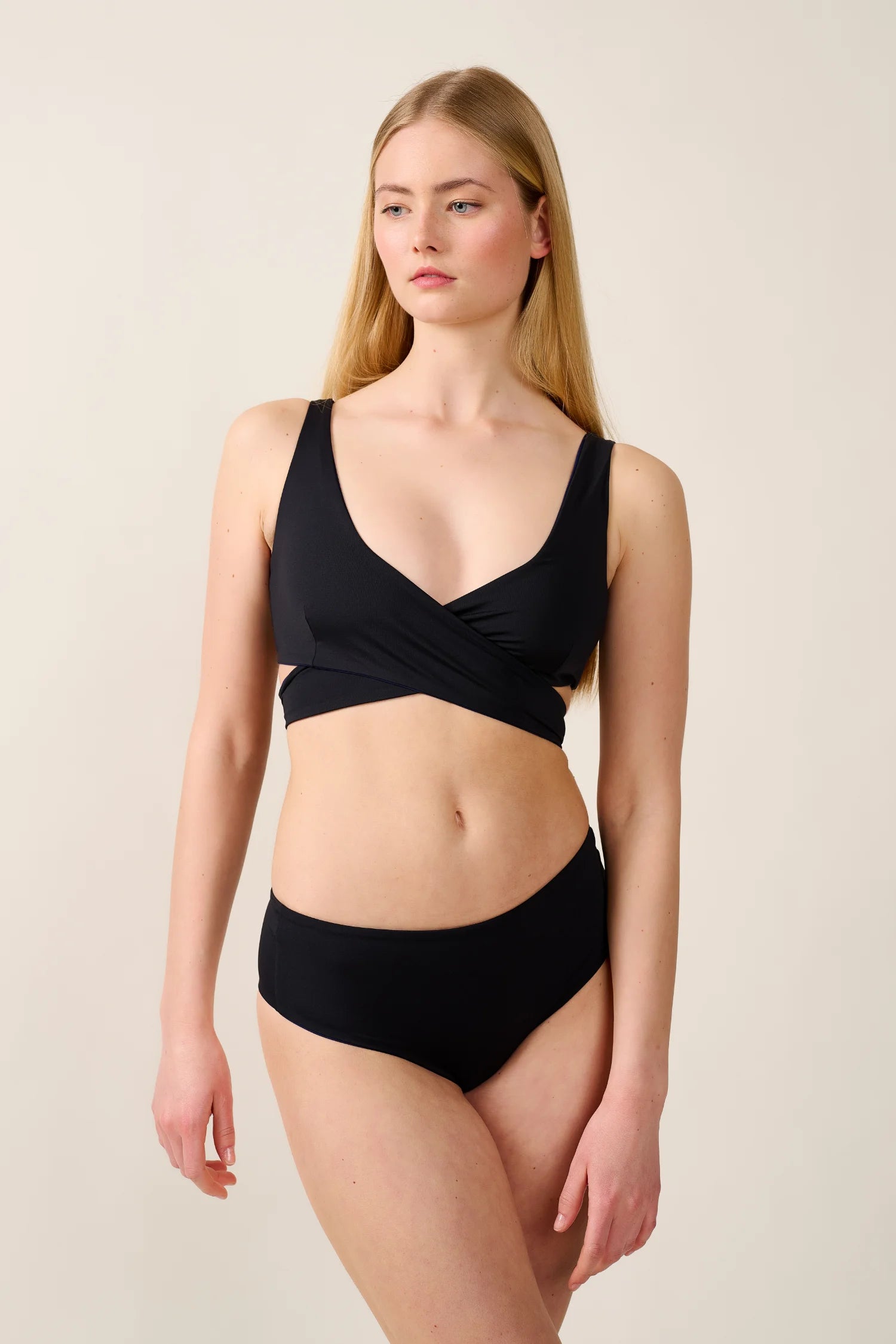 Frau trägt MYMARINI Bikinitop mit V-Ausschnitt und Bikinihose in Schwarz.#color_black-navy