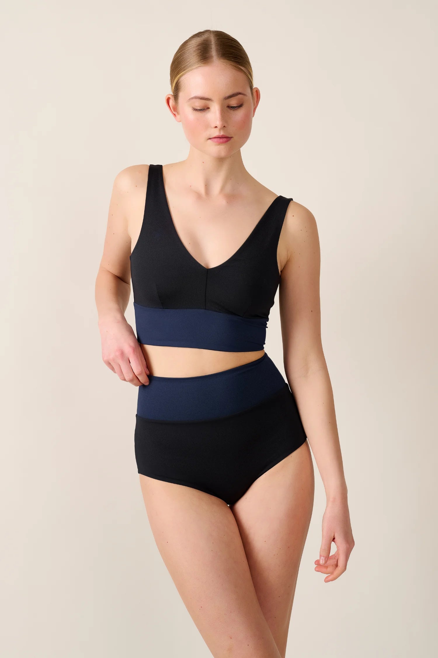 Frau trägt MYMARINI Bikinitop mit V-Ausschnitt und breite Träger, dazu passende High-Waist-Bikinihose in Schwarz und Blau.#color_black-navy
