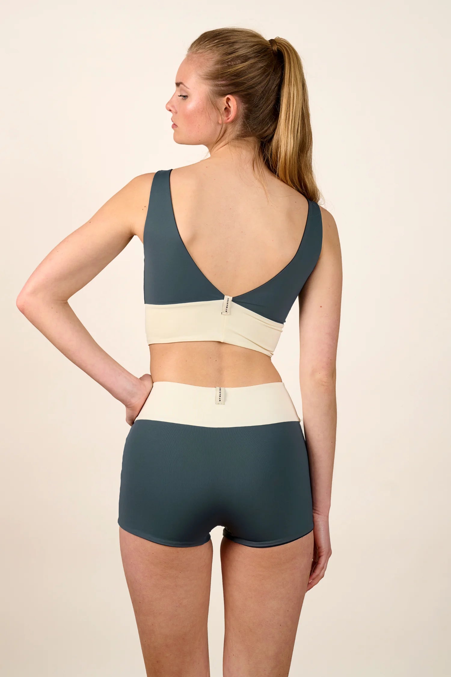 Frau trägt MYMARINI Bikinitop mit V-Ausschnitt und Bikinihose mit High Waist in Blau und Creme.#color_black-grey-white