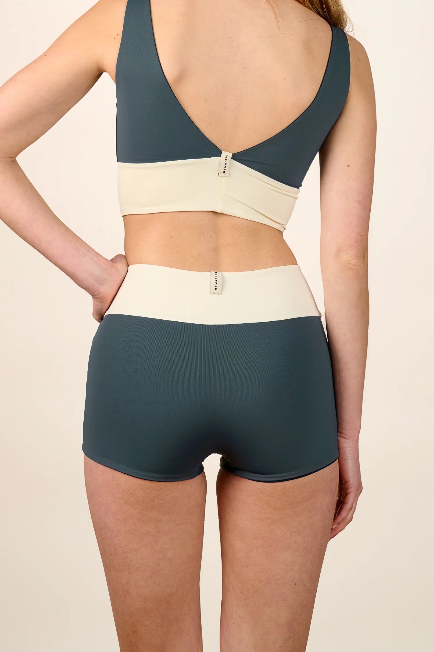 Frau trägt MYMARINI Bikinitop mit V-Ausschnitt und Bikinihose mit High Waist in Blau und Creme.#color_black-grey-white