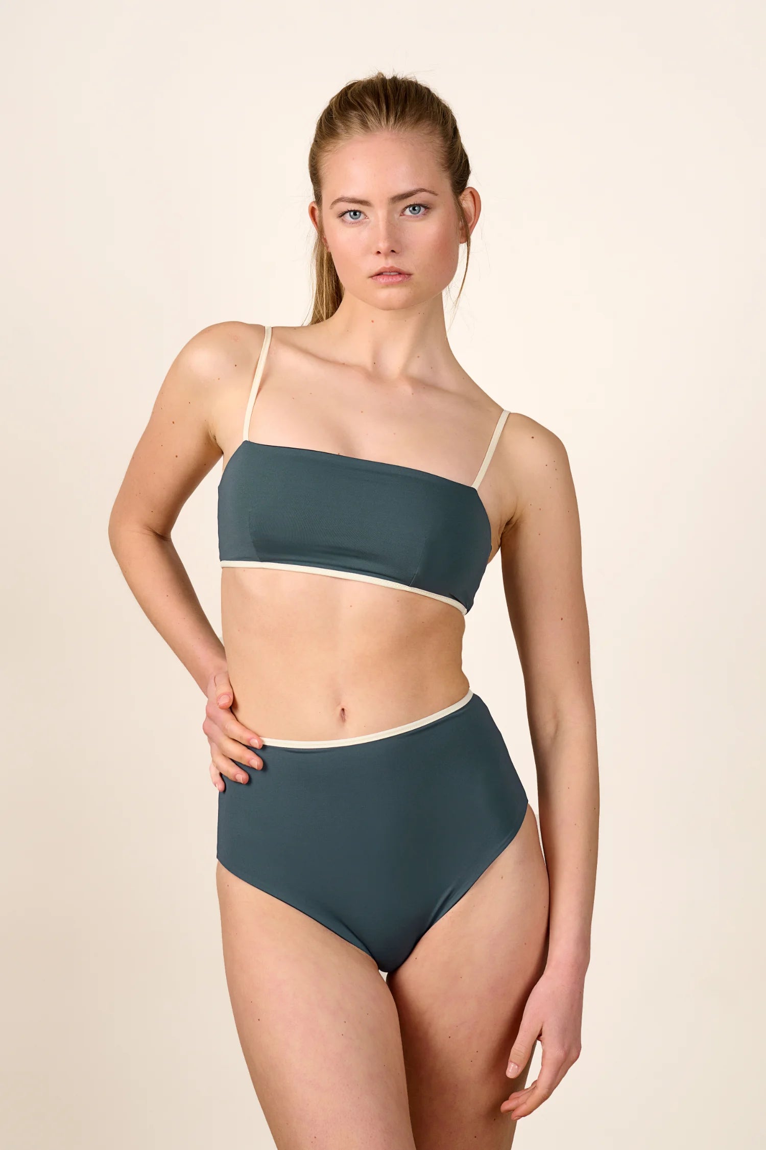 Frau trägt MYMARINI Bikini mit Bandeau-Top und High-Waist-Hose in Dunkelgrün vor hellem Hintergrund.#color_black-grey-white