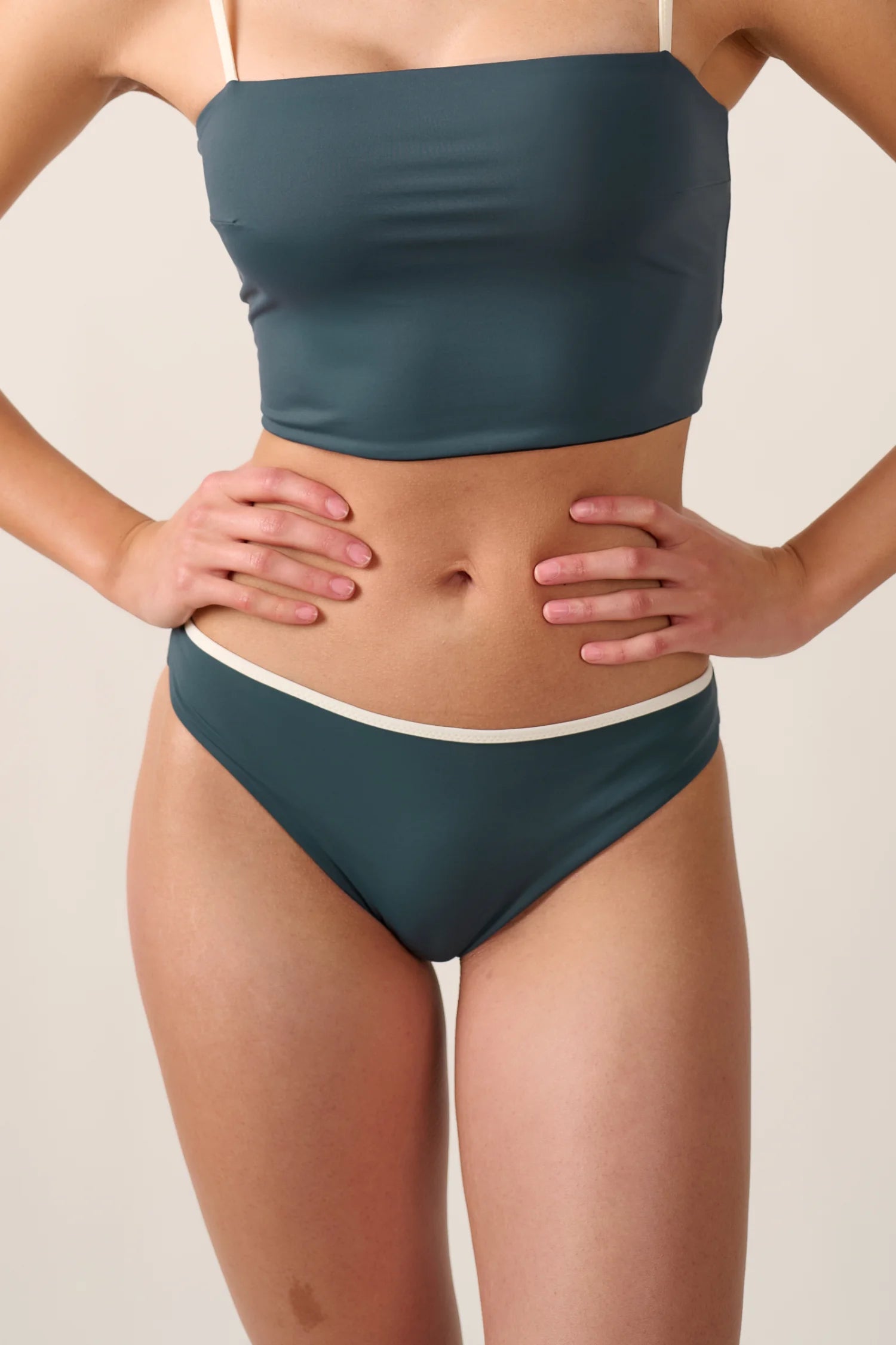 Person trägt MYMARINI Bikini mit Bandeau-Top und Bikinihose in Mid rise. Hände in die Hüften gestützt.#color_black-grey-white