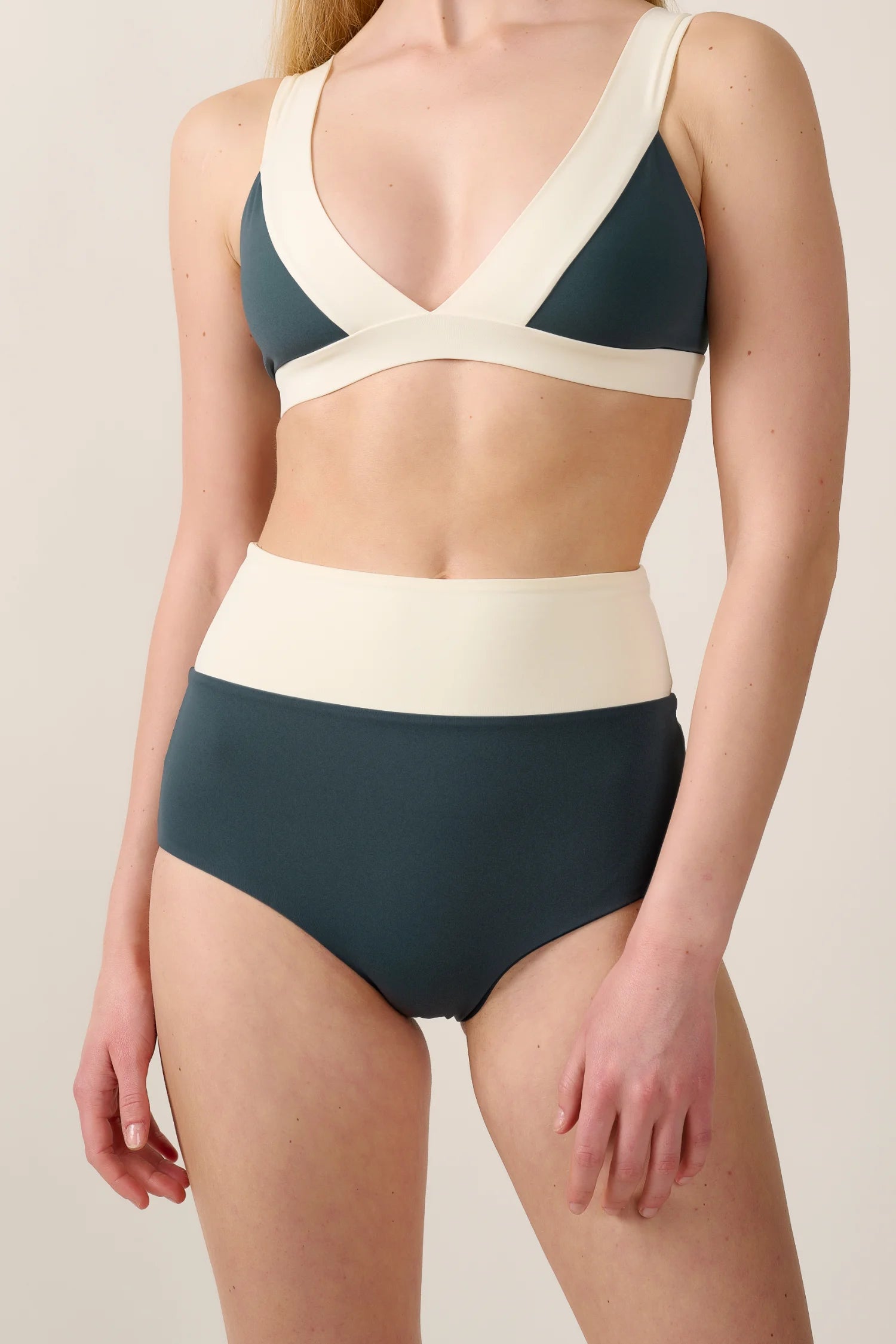 Frau trägt MYMARINI Bikini mit V-Ausschnitt und High Waist Schnitt in Dunkelgrün und Creme.#color_black-grey-white