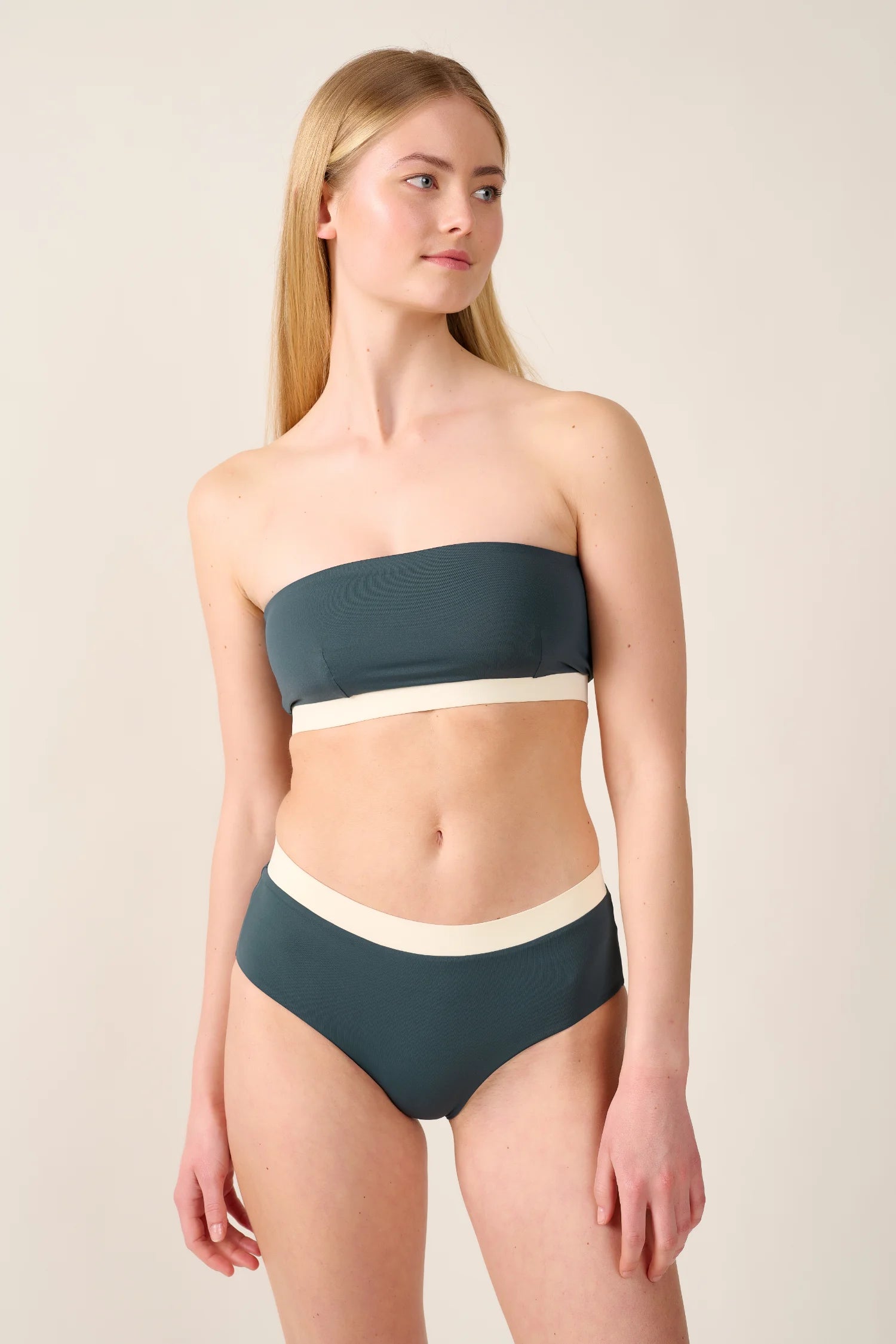 Frau trägt MYMARINI Bandeau-Bikinitop und High-Waist-Bikinihose in Dunkelgrün mit cremefarbenen Details.#color_black-grey-white