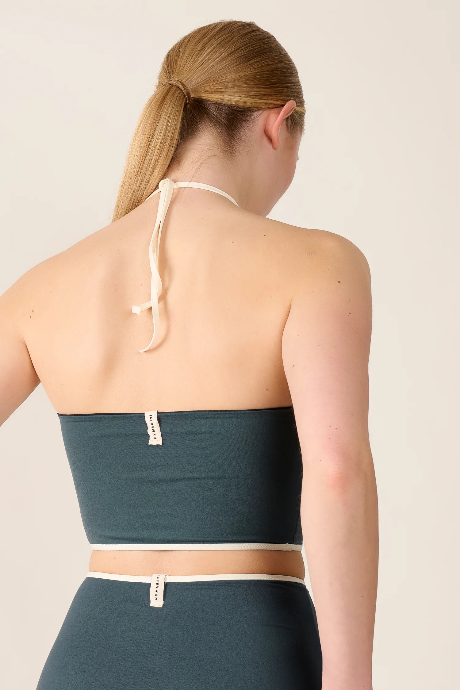 Frau von hinten in MYMARINI-Bikini mit Bandeau-Top und Neckholder-Trägern in Dunkelgrün.#color_black-grey-white