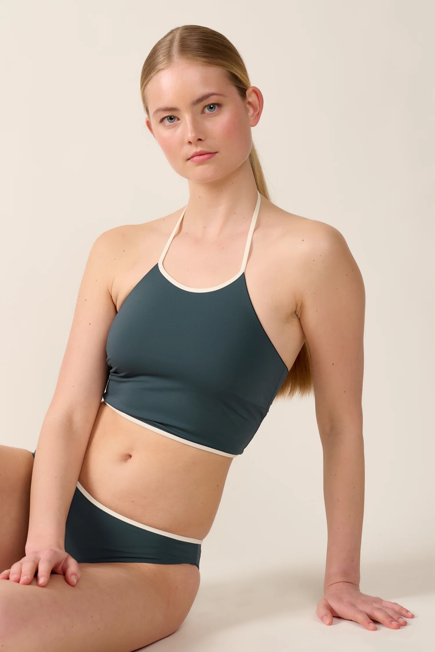 Frau in MYMARINI Bikinitop mit Neckholder und Bikinihose, sitzt vor neutralem Hintergrund.#color_black-grey-white