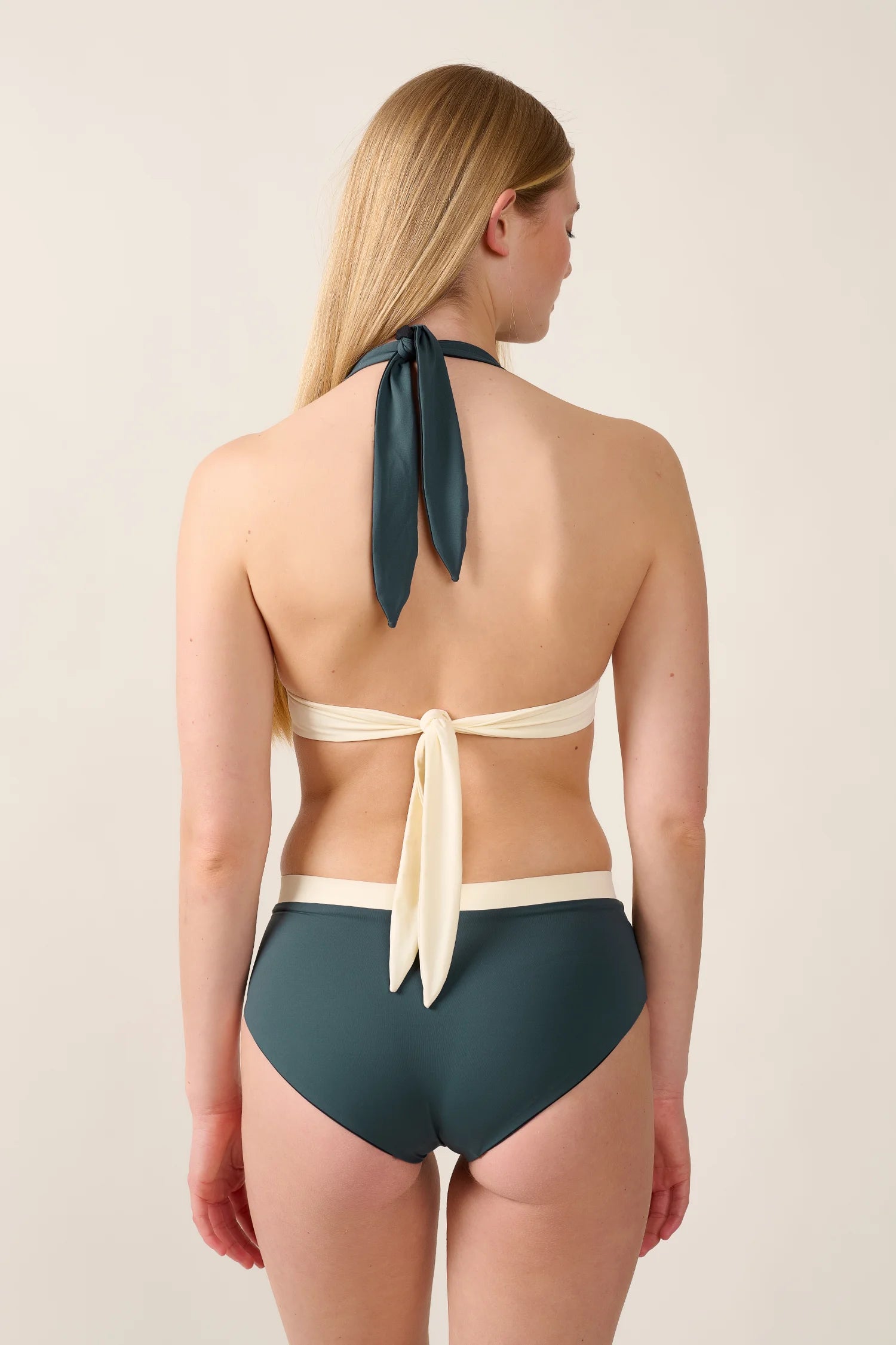 Frau trägt MYMARINI Bikini mit Neckholder und hohem Beinausschnitt in Dunkelgrün und Creme, Rückansicht.#color_black-grey-white